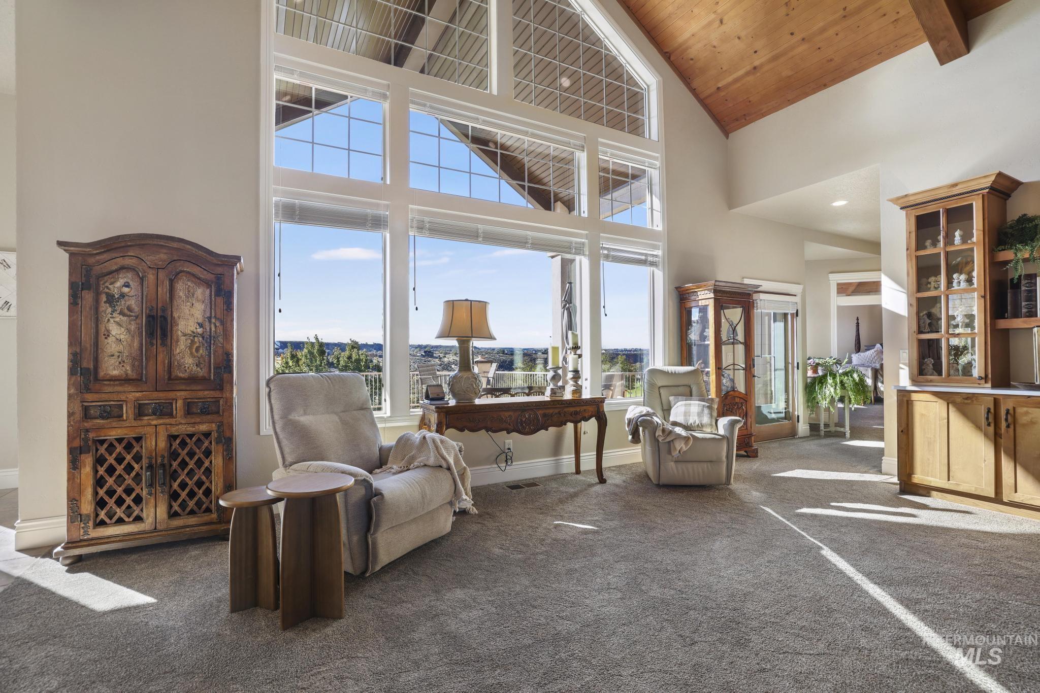 Living area with high vaulted ceiling, dark carpet, and a wooden ceiling with exposed beams