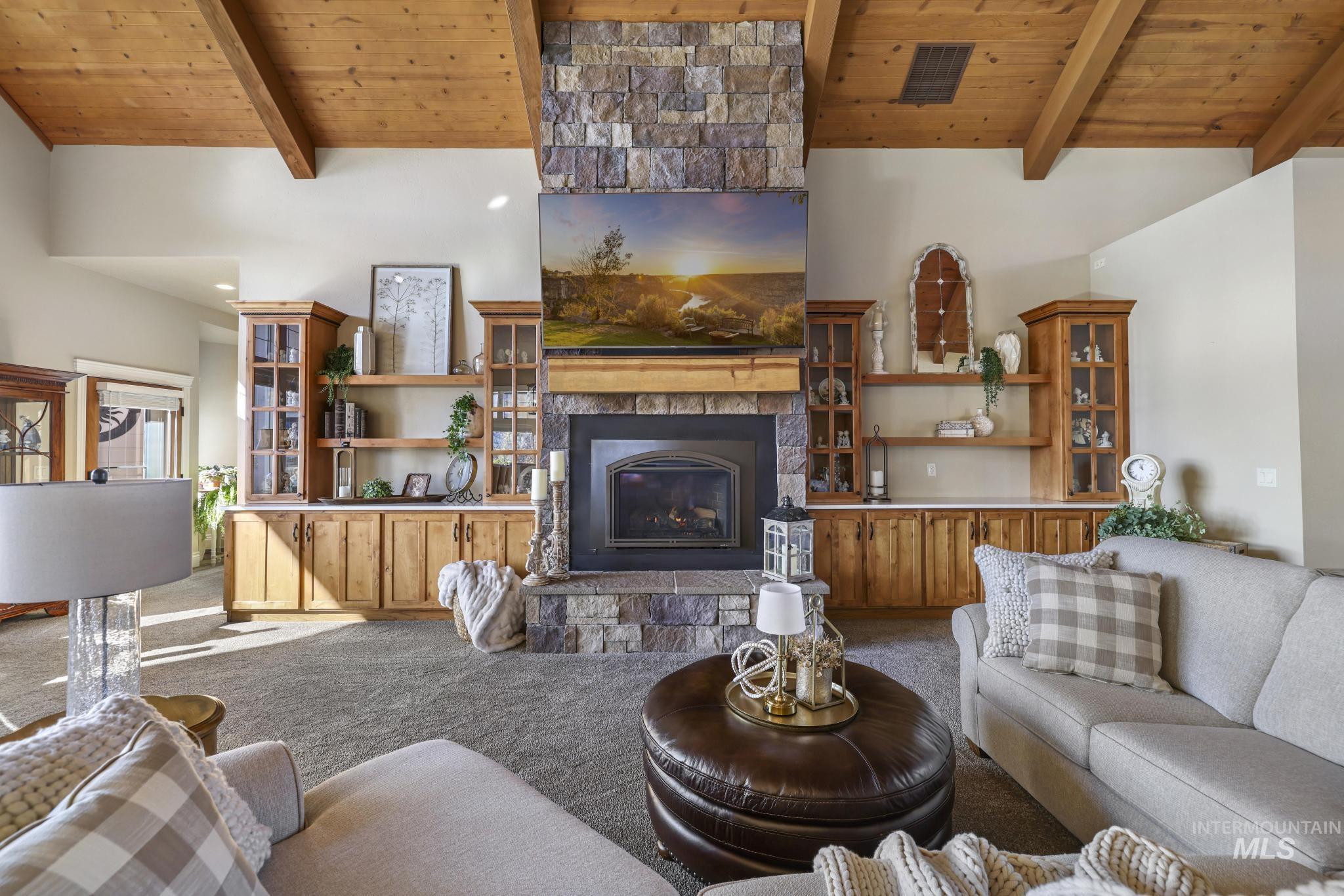 Carpeted living area with a wood ceiling with exposed beams, high vaulted ceiling, and a stone fireplace
