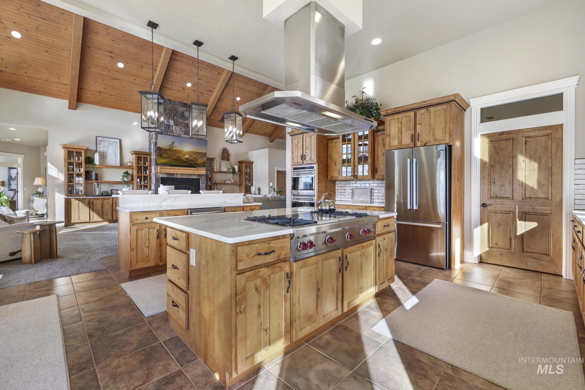 Kitchen featuring open floor plan, island range hood, stainless steel appliances, glass insert cabinets, and decorative light fixtures