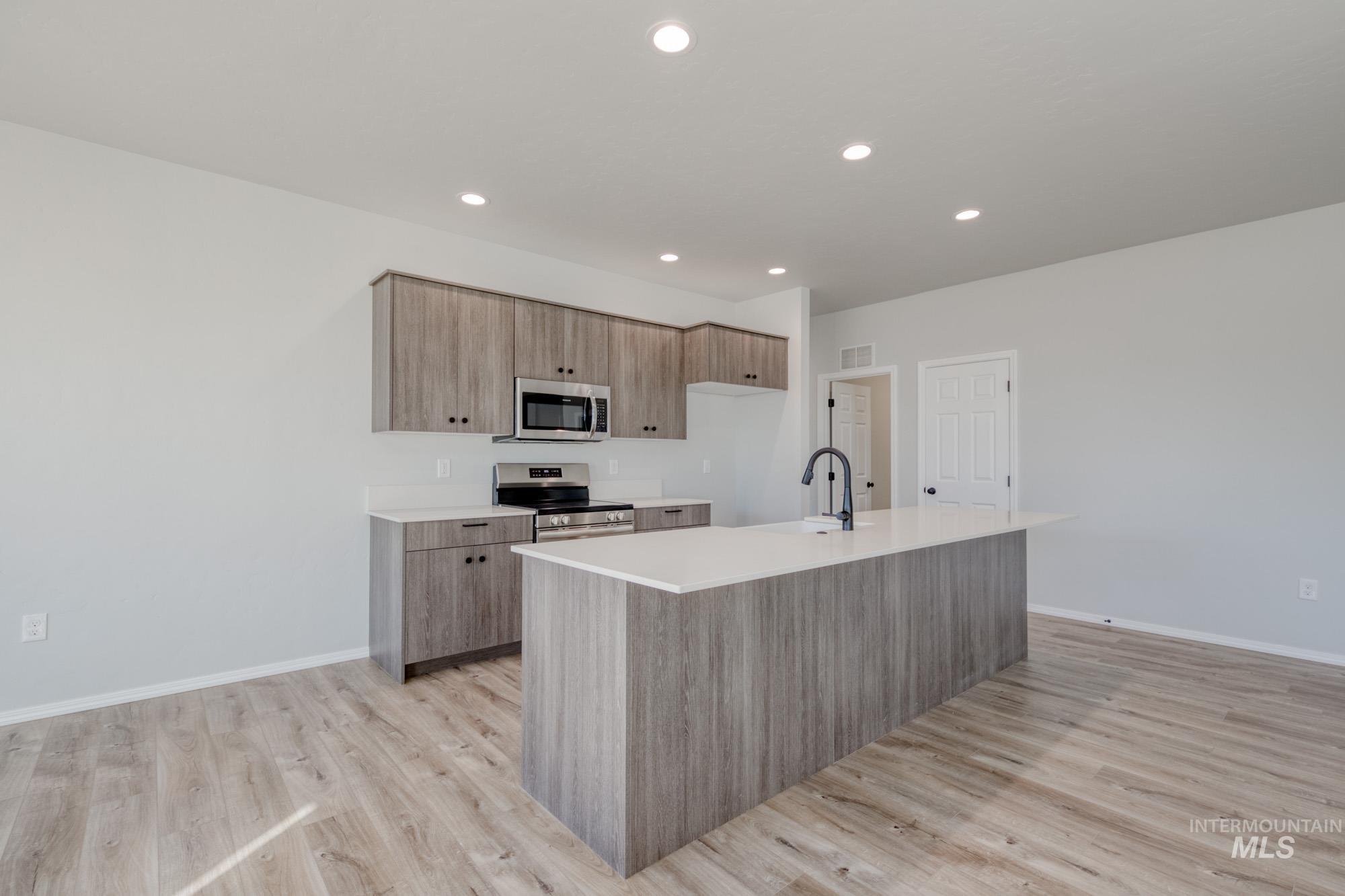 Kitchen with an island with sink, stainless steel appliances, light wood finished floors, recessed lighting, and modern cabinets