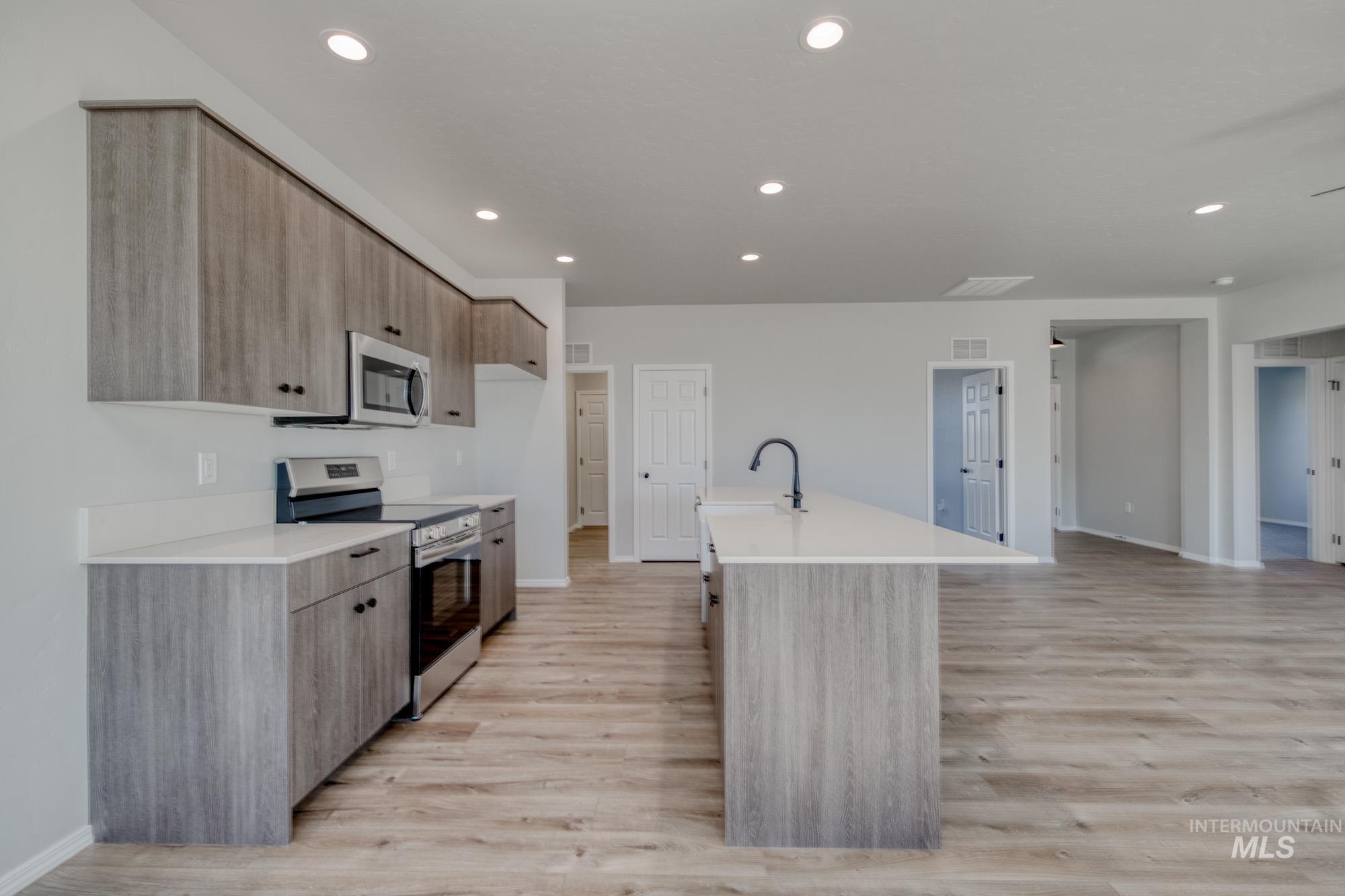 Kitchen featuring modern cabinets, stainless steel appliances, recessed lighting, light wood-style flooring, and a kitchen island with sink