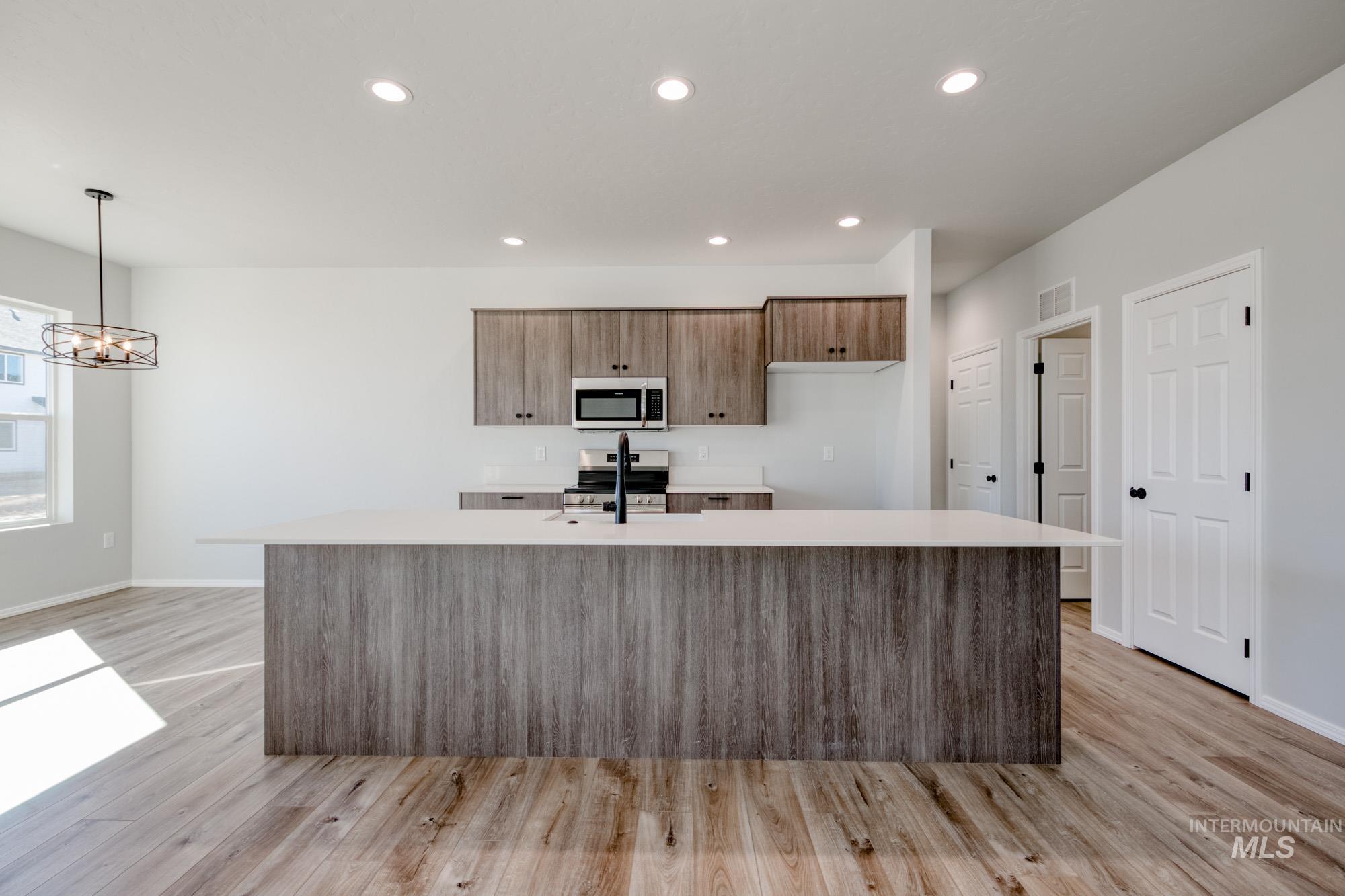 Kitchen featuring stainless steel appliances, a kitchen island with sink, light wood-style flooring, recessed lighting, and brown cabinets