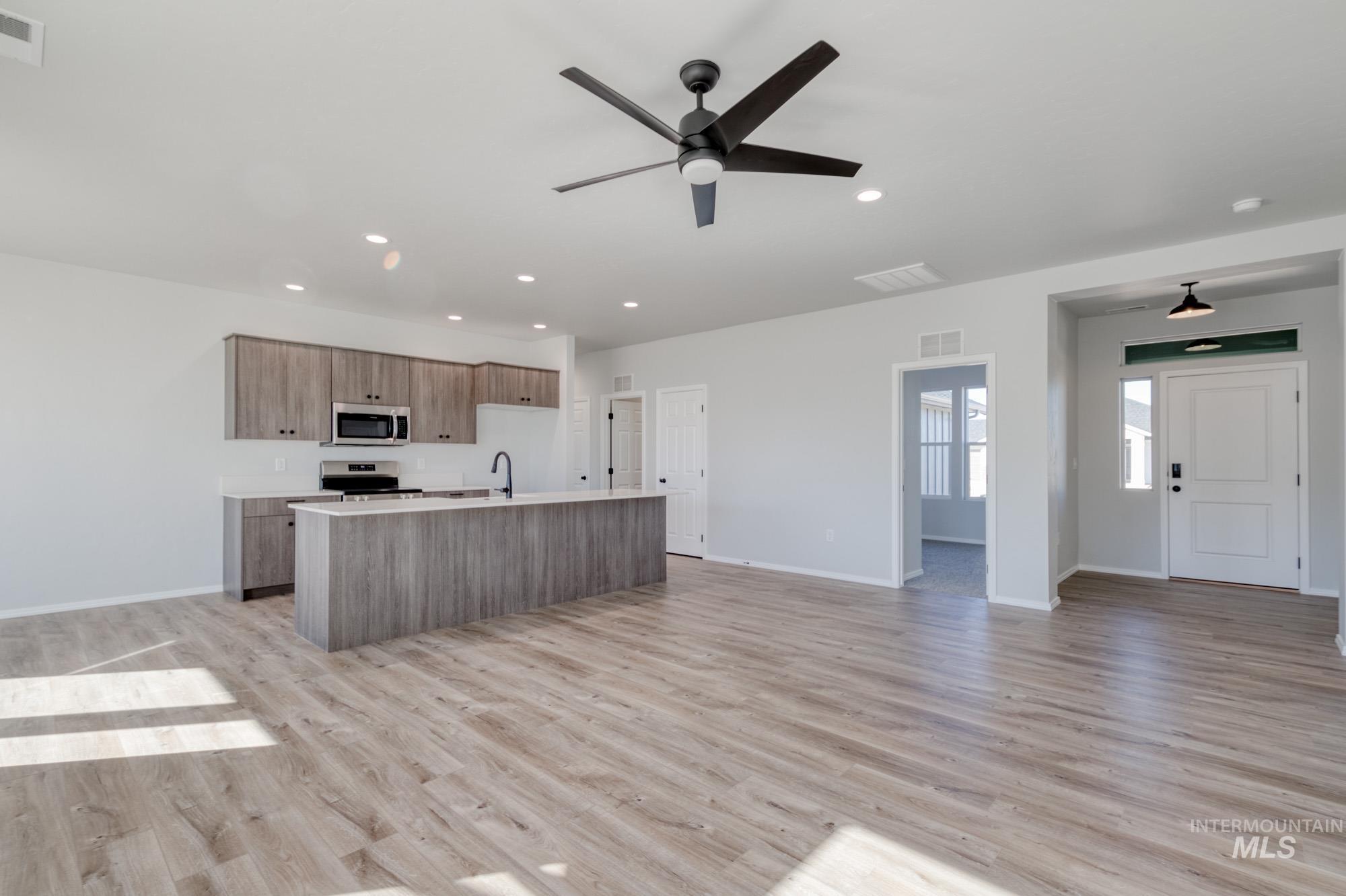 Kitchen featuring open floor plan, an island with sink, light wood-style flooring, stainless steel appliances, and ceiling fan