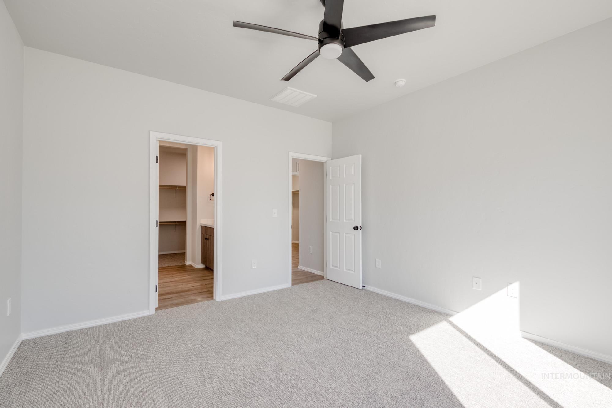 Unfurnished bedroom with a walk in closet, light colored carpet, ceiling fan, and connected bathroom