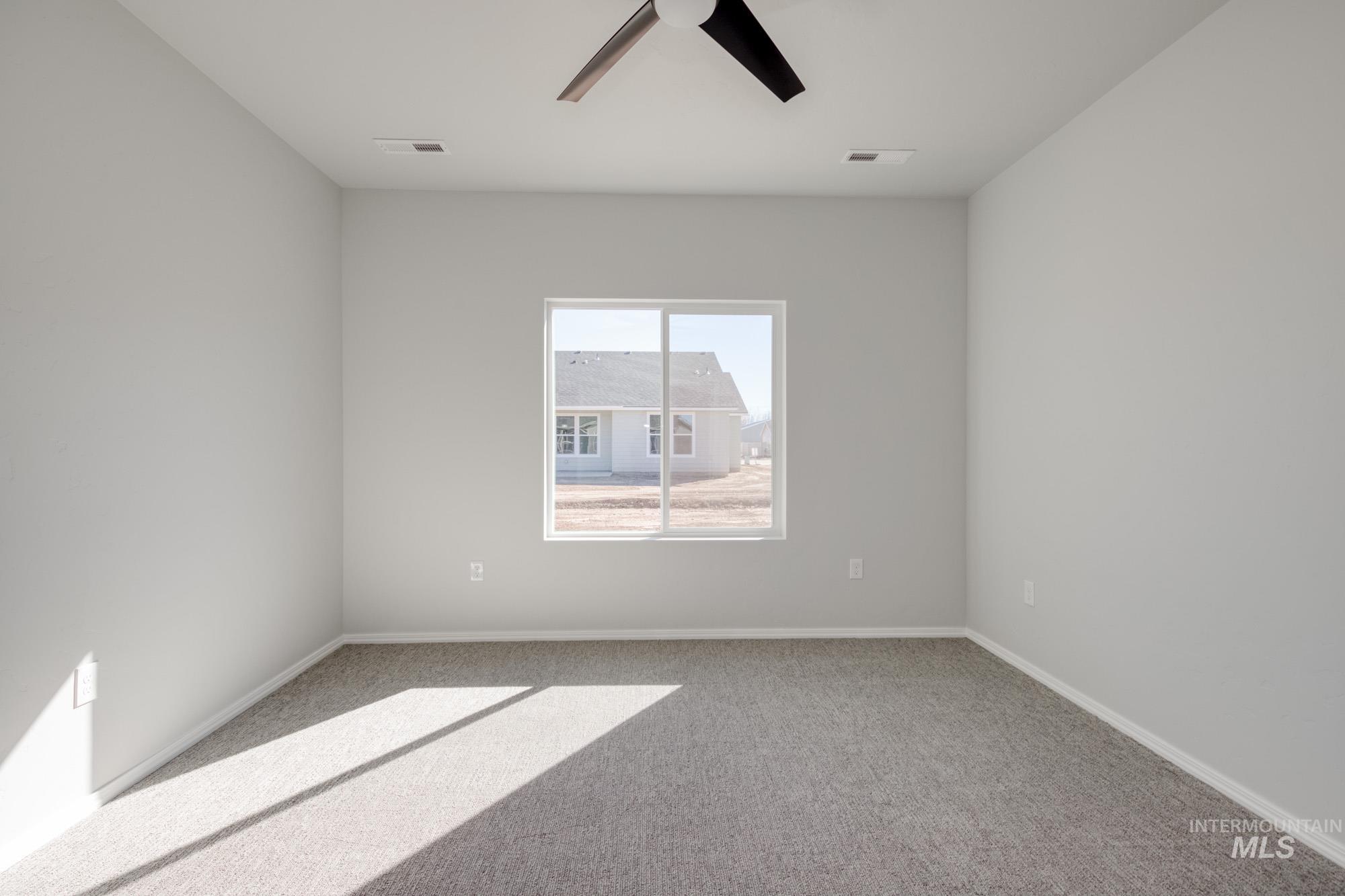 Carpeted spare room featuring a ceiling fan and baseboards