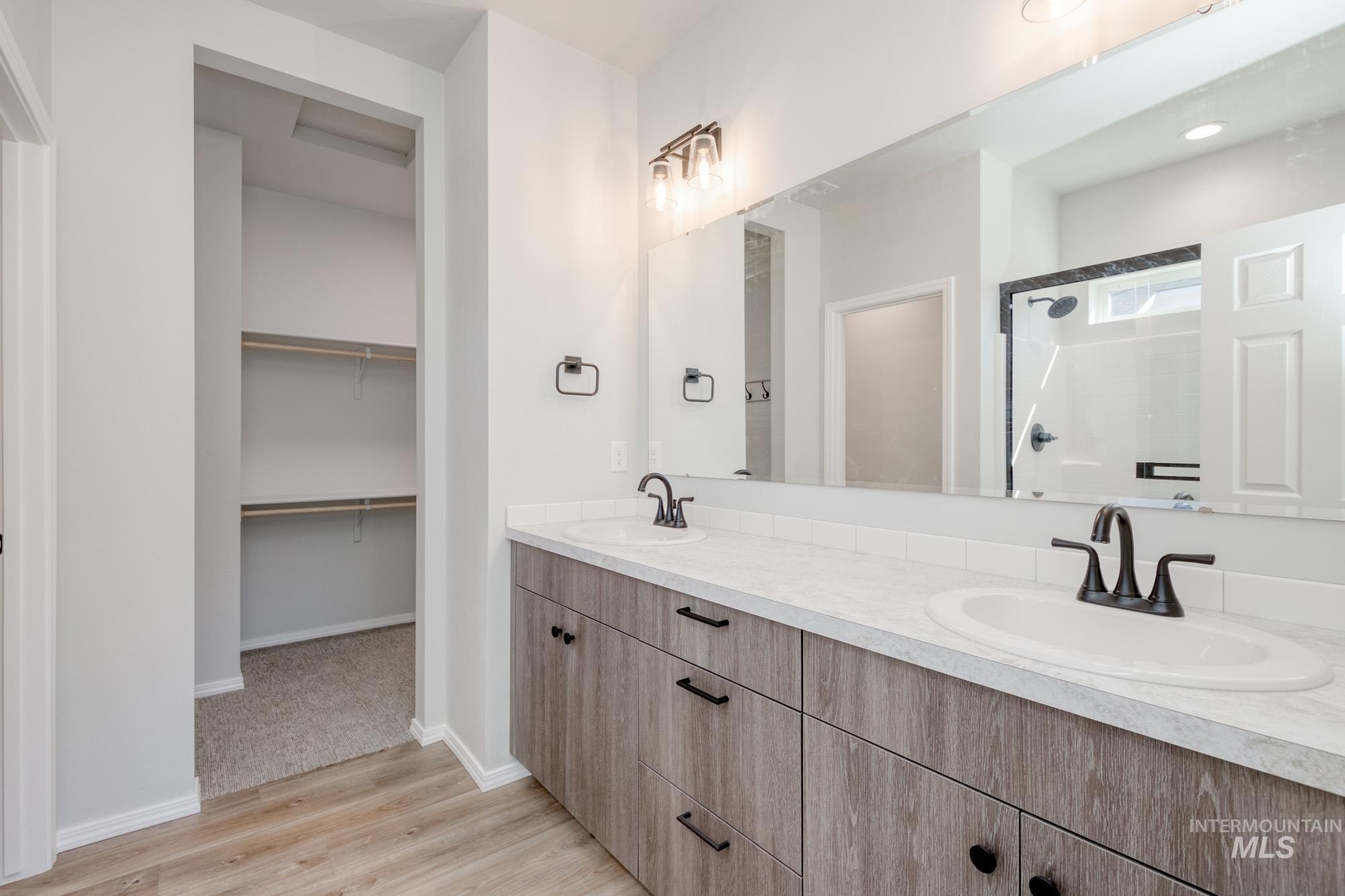 Full bath featuring light wood finished floors, a shower stall, double vanity, and a walk in closet