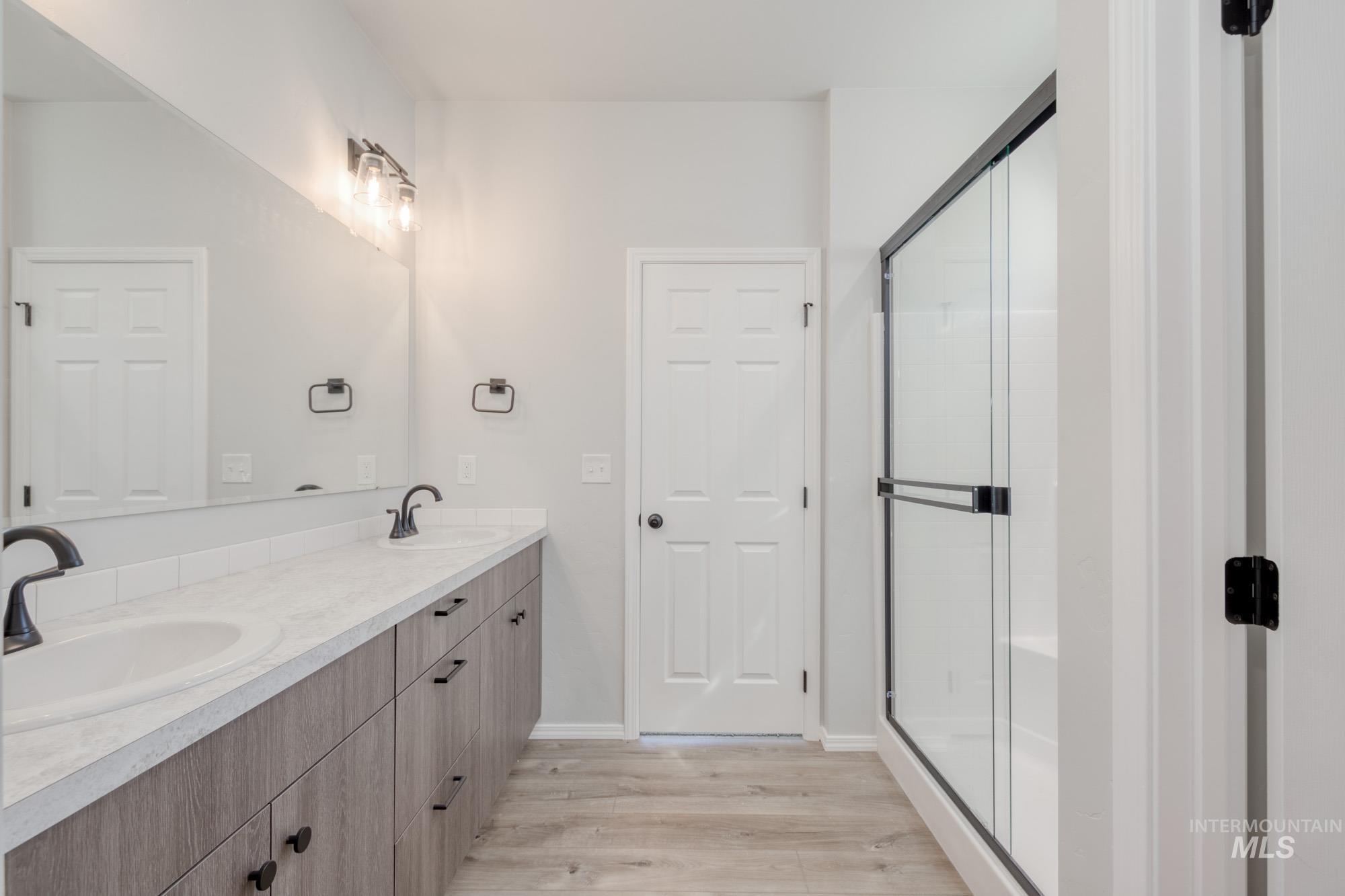Bathroom featuring double vanity, light wood finished floors, and a stall shower