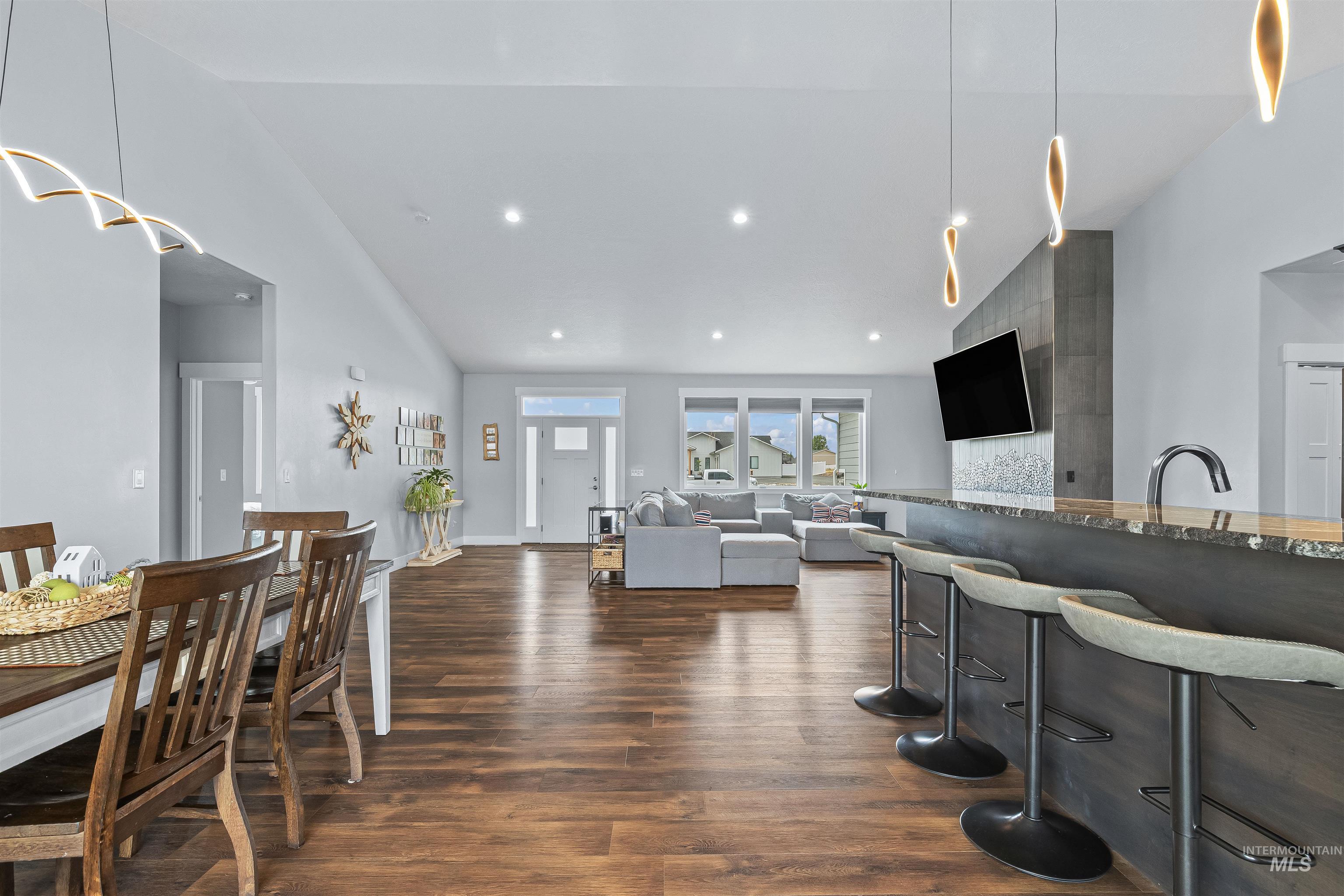 Kitchen featuring high vaulted ceiling, dark wood-type flooring, stone countertops, recessed lighting, and a kitchen bar