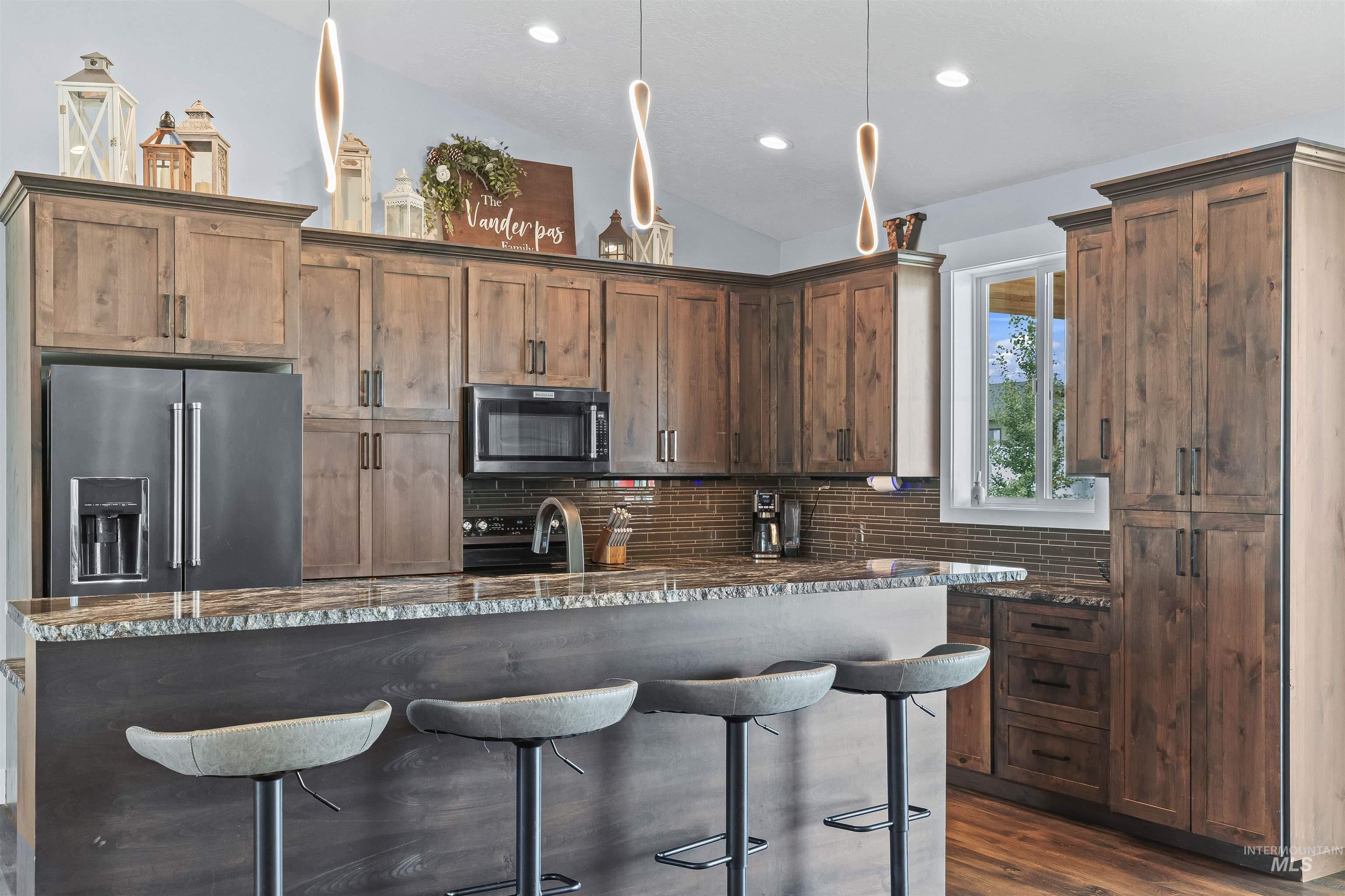 Kitchen with high quality fridge, lofted ceiling, dark stone countertops, a breakfast bar, and decorative backsplash