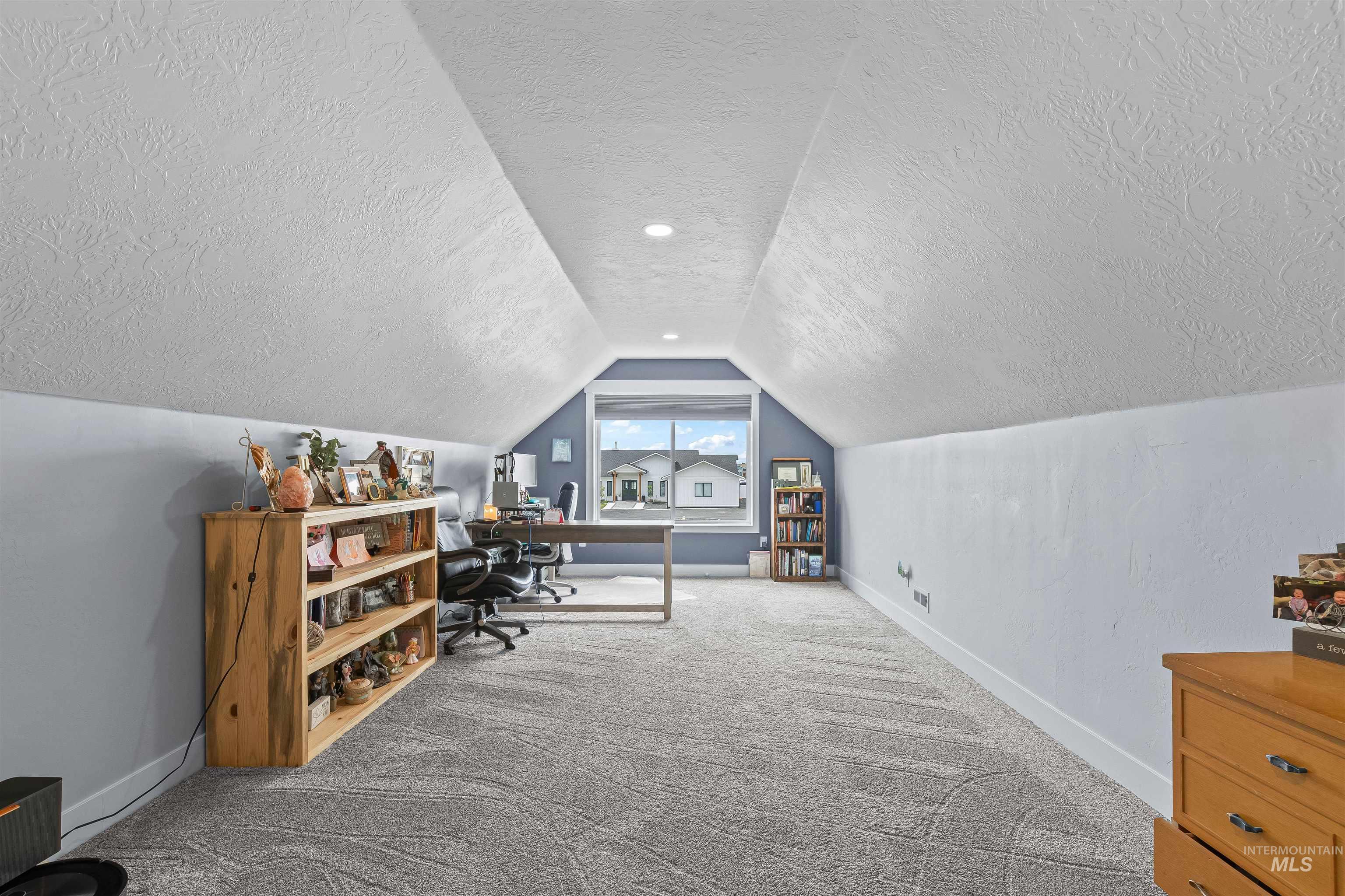 Carpeted home office featuring a textured ceiling and vaulted ceiling