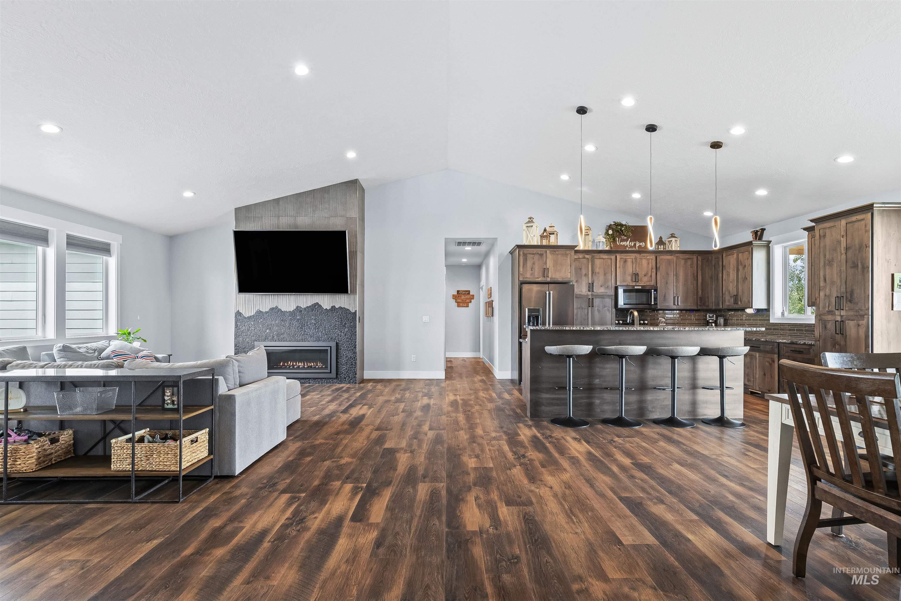 Living room featuring dark wood-style flooring, vaulted ceiling, a large fireplace, and recessed lighting