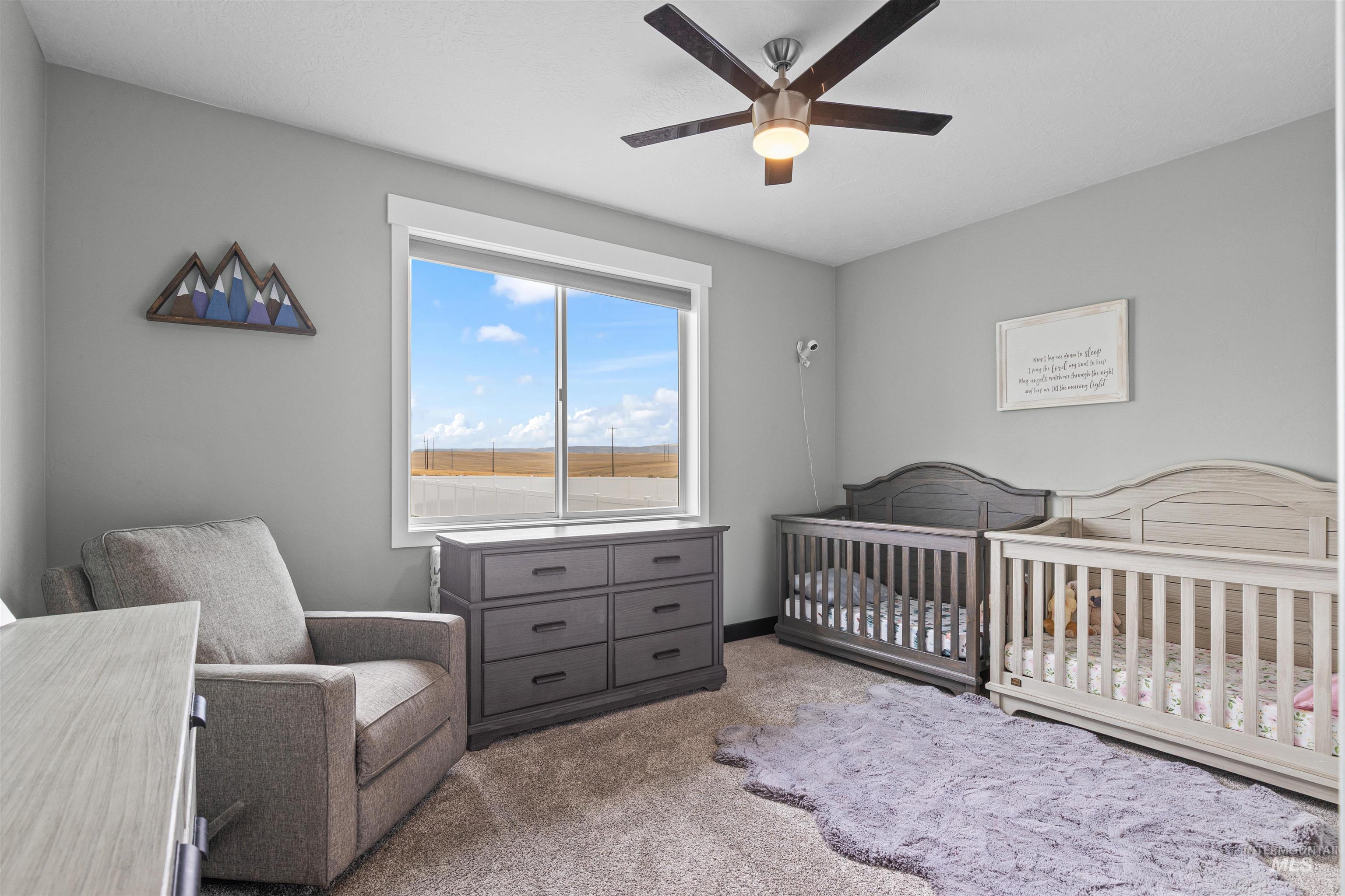 Carpeted bedroom featuring a nursery area and ceiling fan