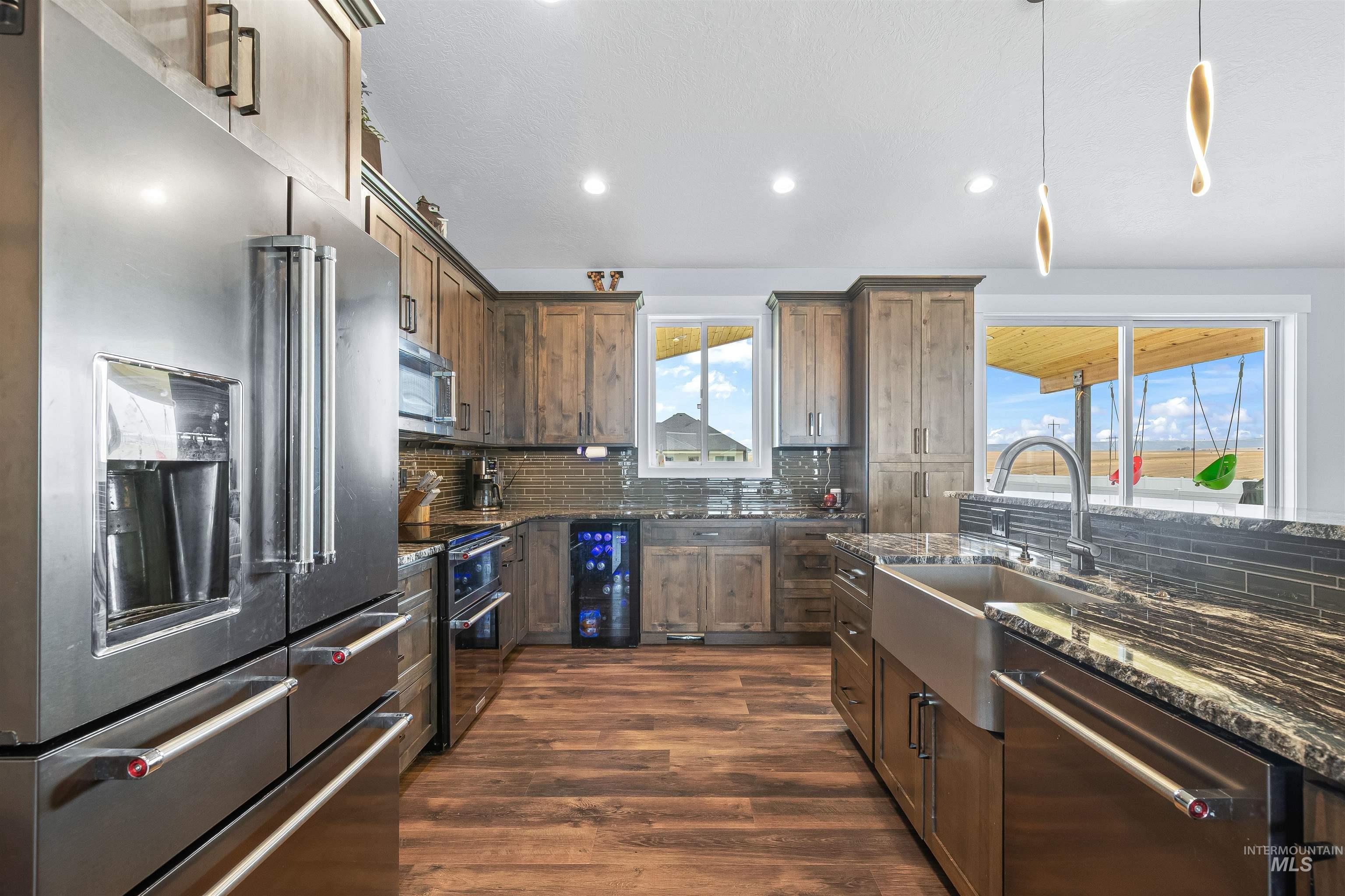 Kitchen featuring stainless steel appliances, tasteful backsplash, dark stone counters, dark wood-style floors, and recessed lighting