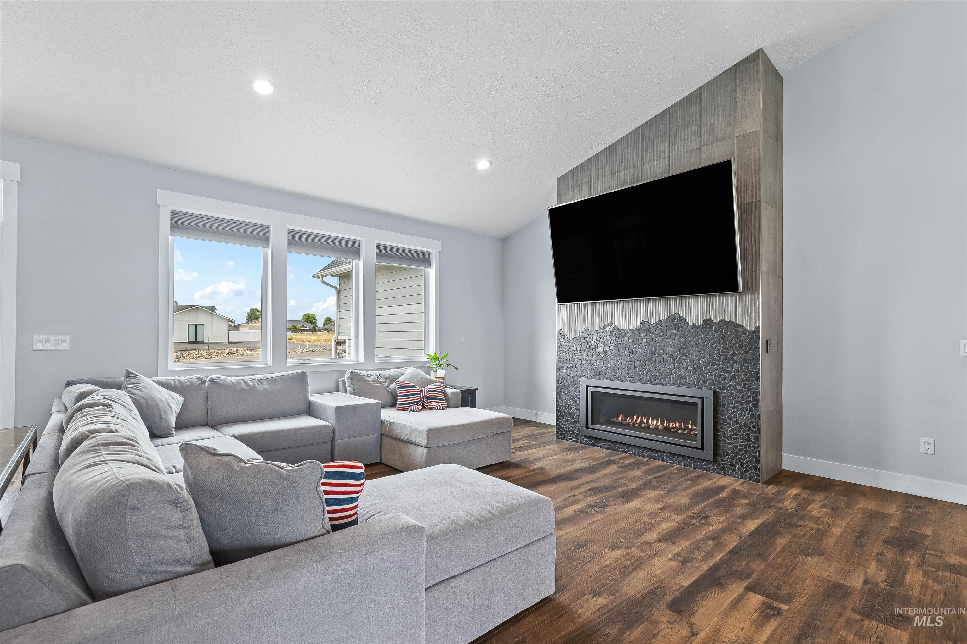 Living room featuring vaulted ceiling, dark wood-style flooring, a tiled fireplace, and recessed lighting