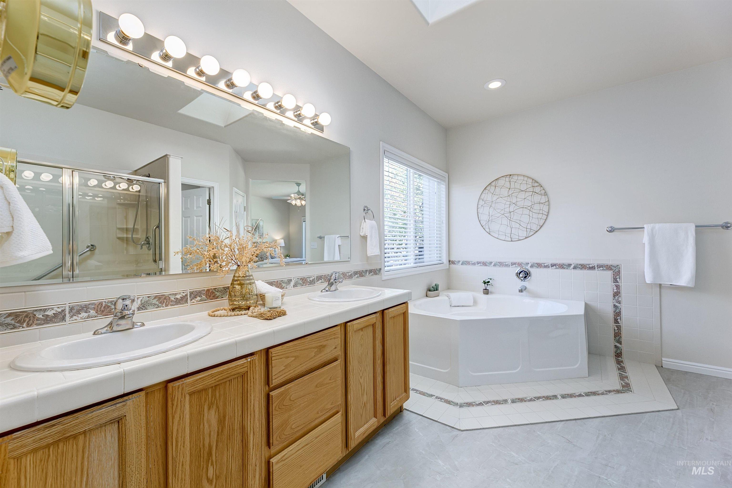 Full bath featuring a skylight, a bath, a stall shower, double vanity, and recessed lighting