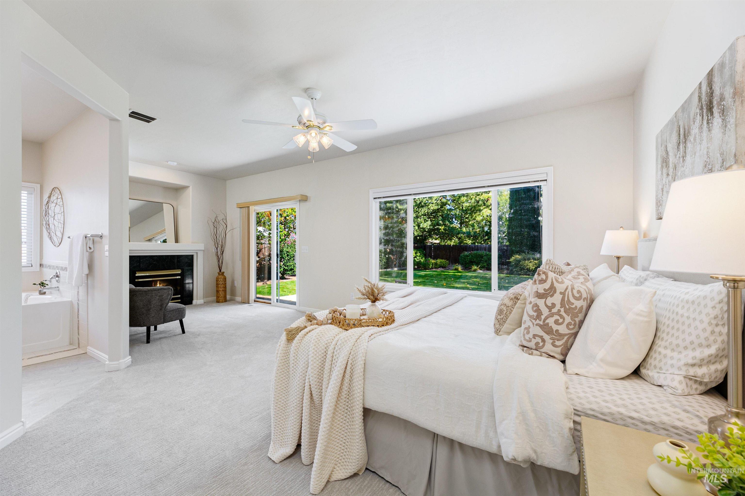 Carpeted bedroom featuring ensuite bathroom, a premium fireplace, and a ceiling fan