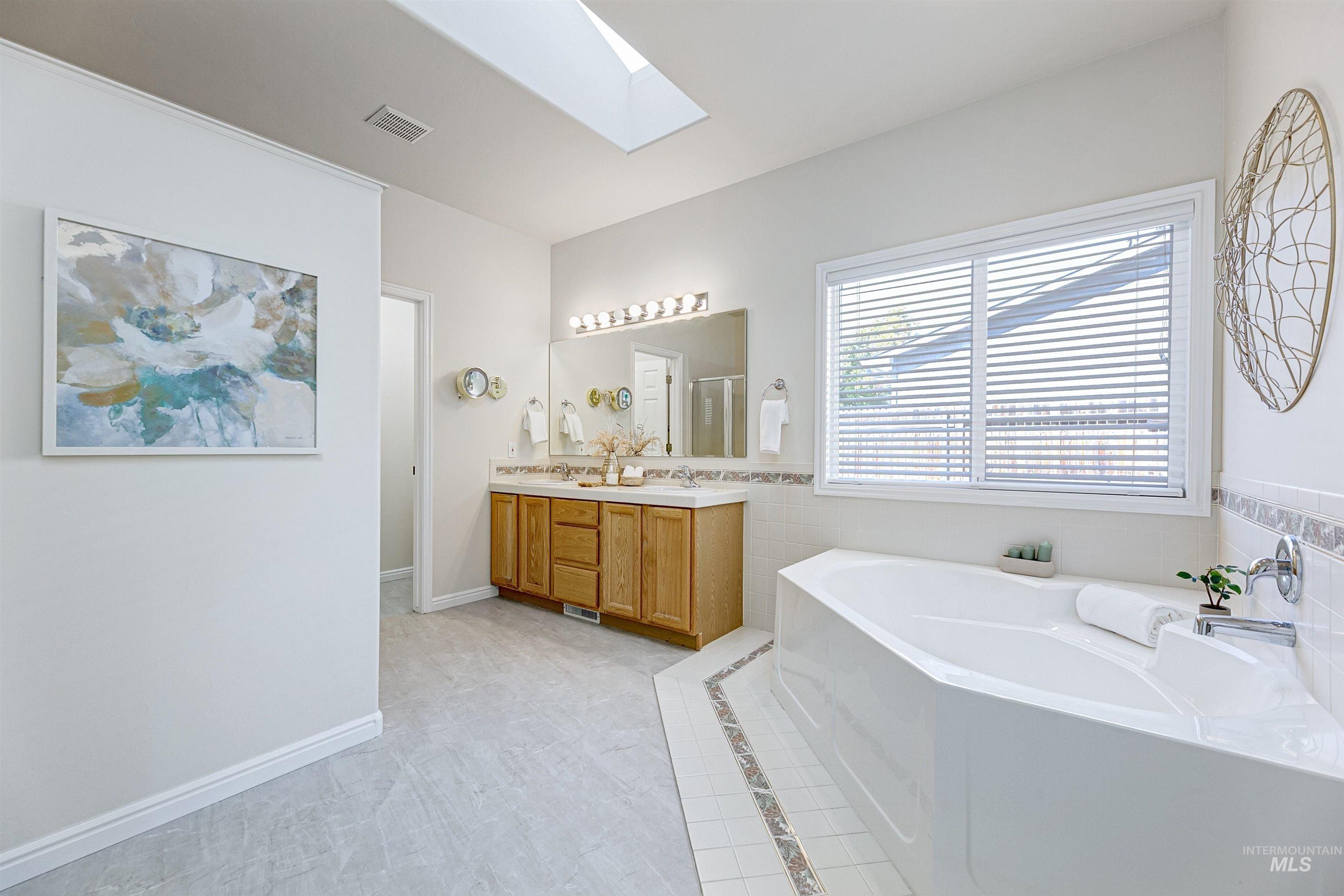Bathroom with a skylight, a garden tub, double vanity, light tile patterned flooring, and tile walls