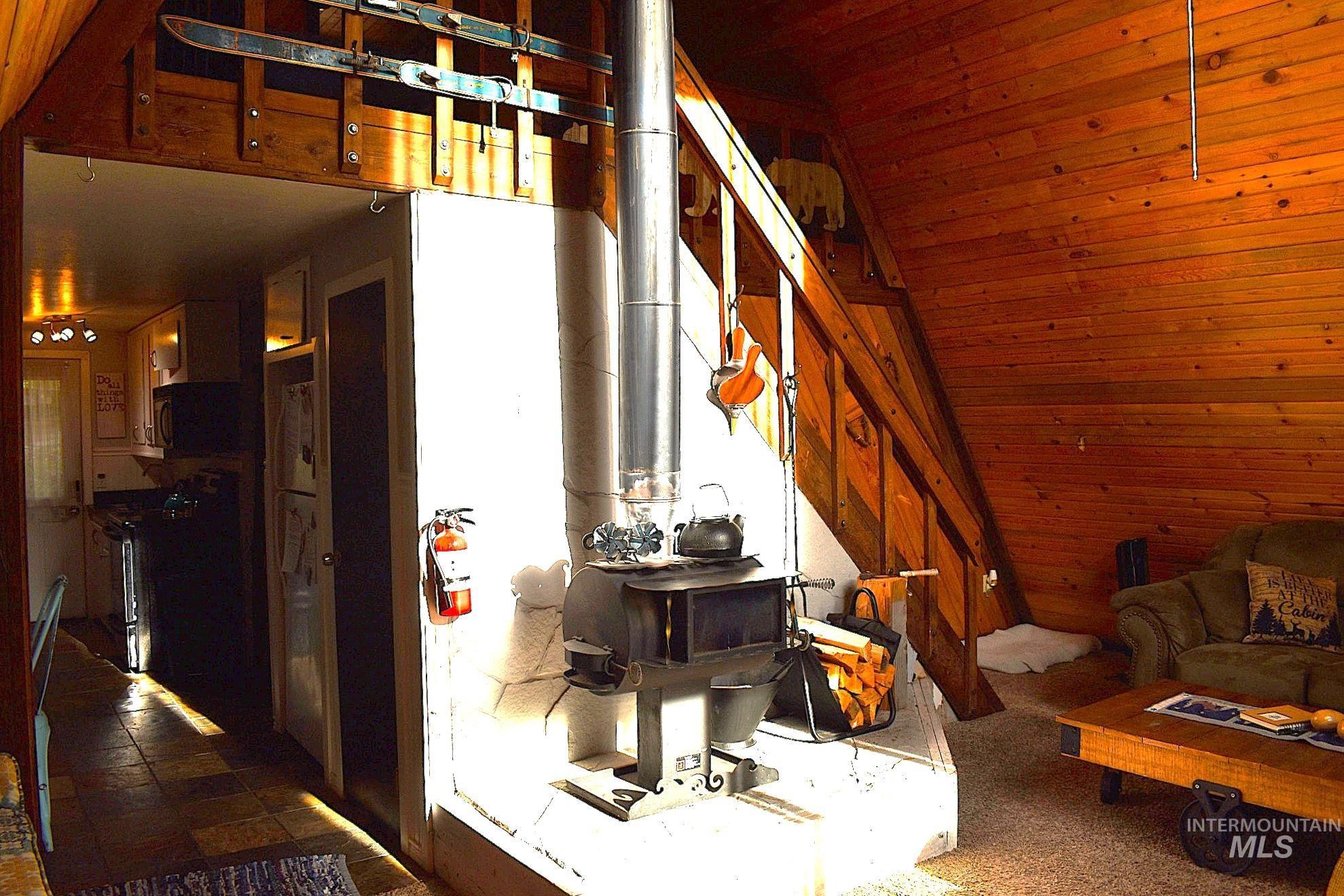 Interior space featuring a wood-paneled wall, exposed wood beams, and a wood-burning stove with a metal flue