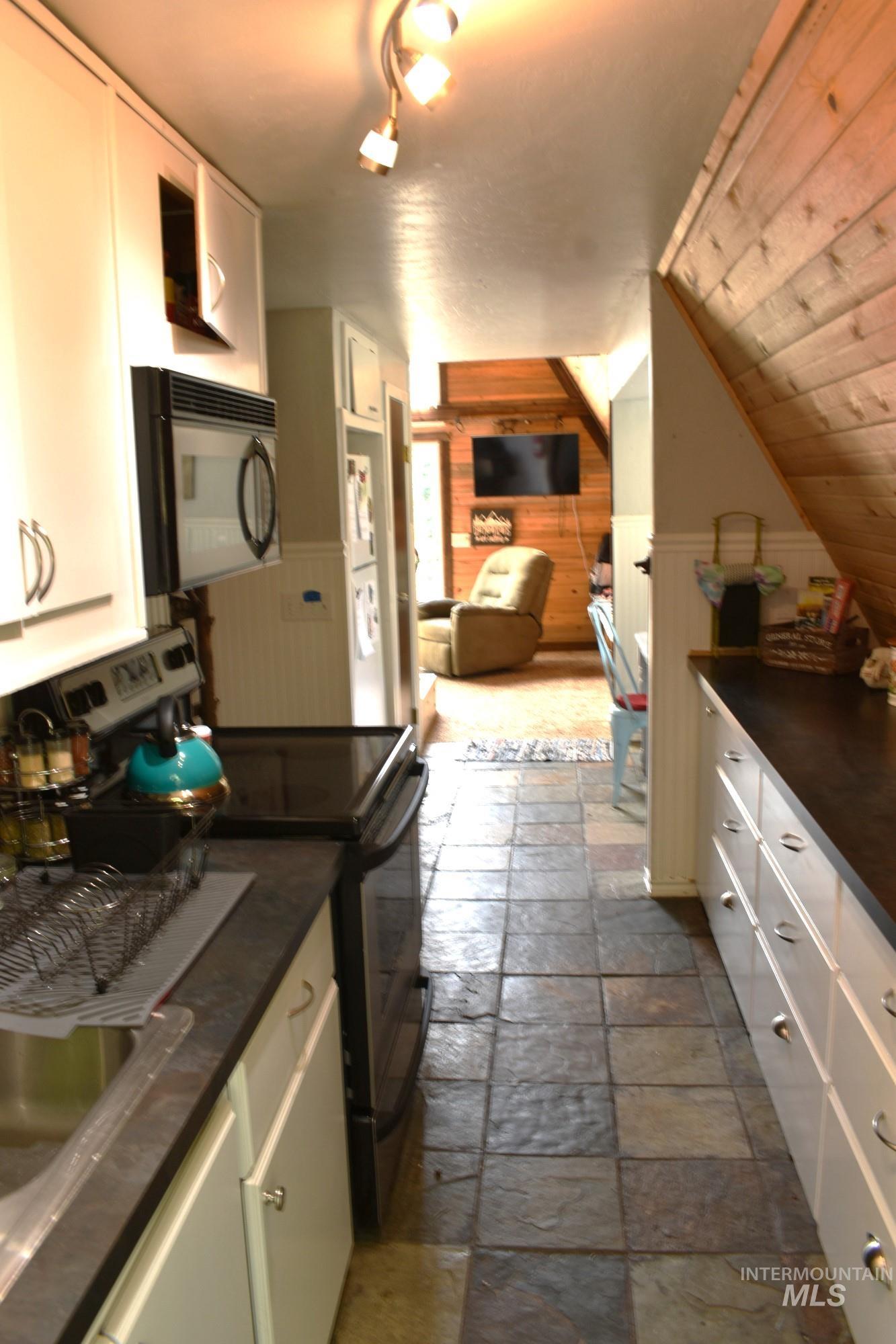 Galley kitchen featuring white cabinetry, dark countertops, and large format tile flooring