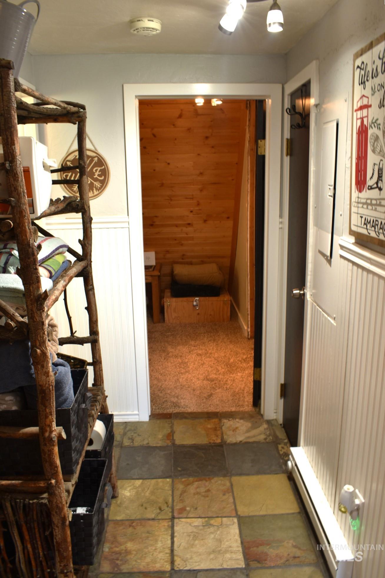 Multicolor slate tile flooring entry featuring white beadboard wainscoting and a doorway opening to a carpeted interior space with wood-paneled walls