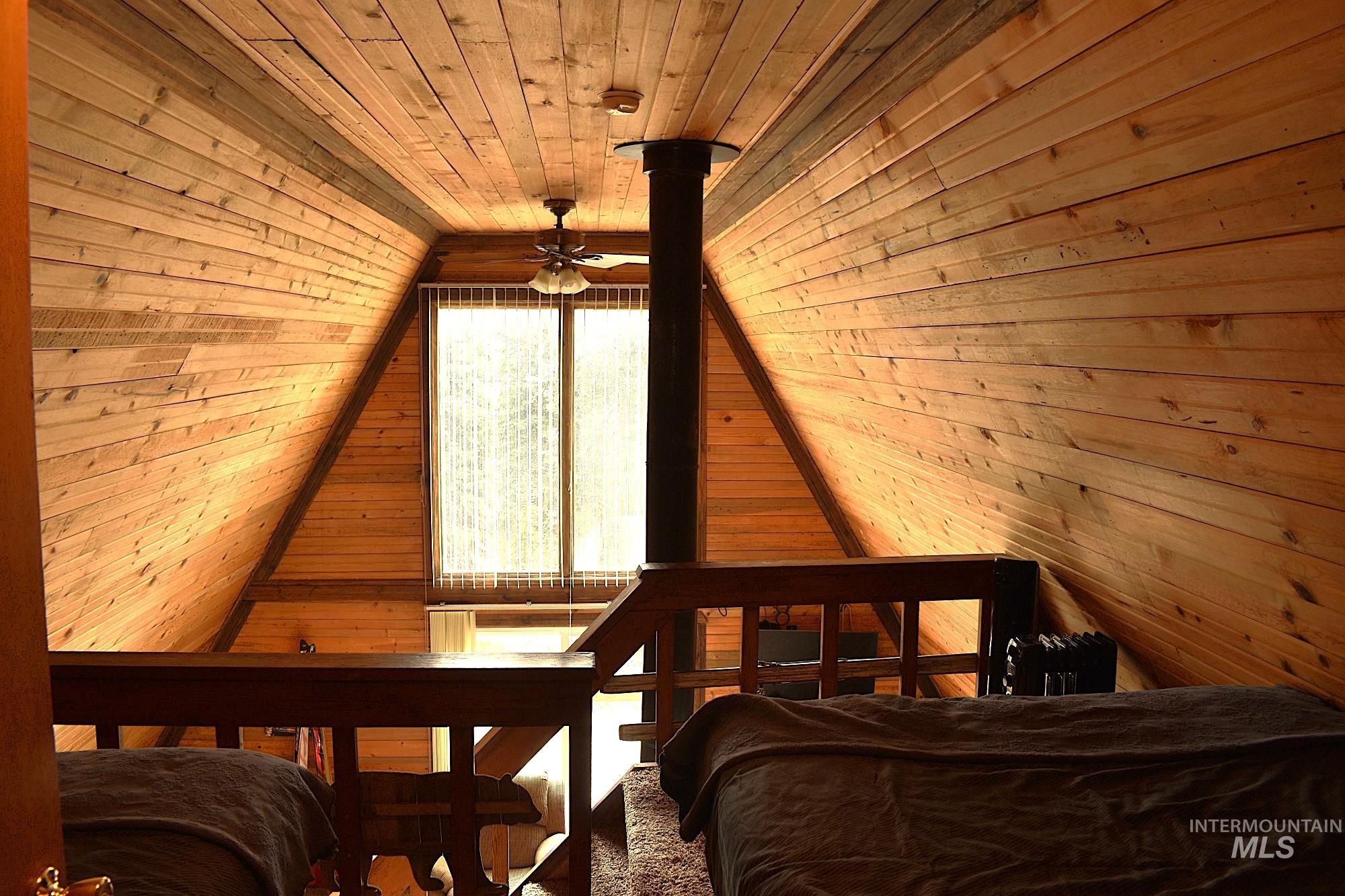 Loft area featuring extensive wood-finish wall and ceiling paneling, a prominent A-frame architectural design, and a ceiling-mounted fan