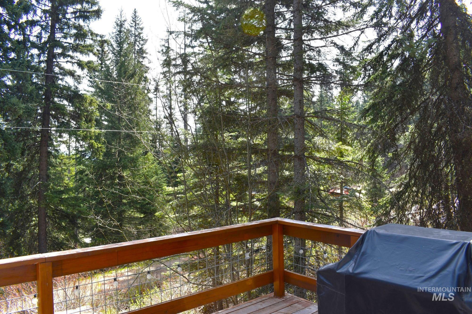 Outdoor deck featuring wood-finish flooring and a wood-finish railing with metal wire infill, surrounded by mature evergreen trees
