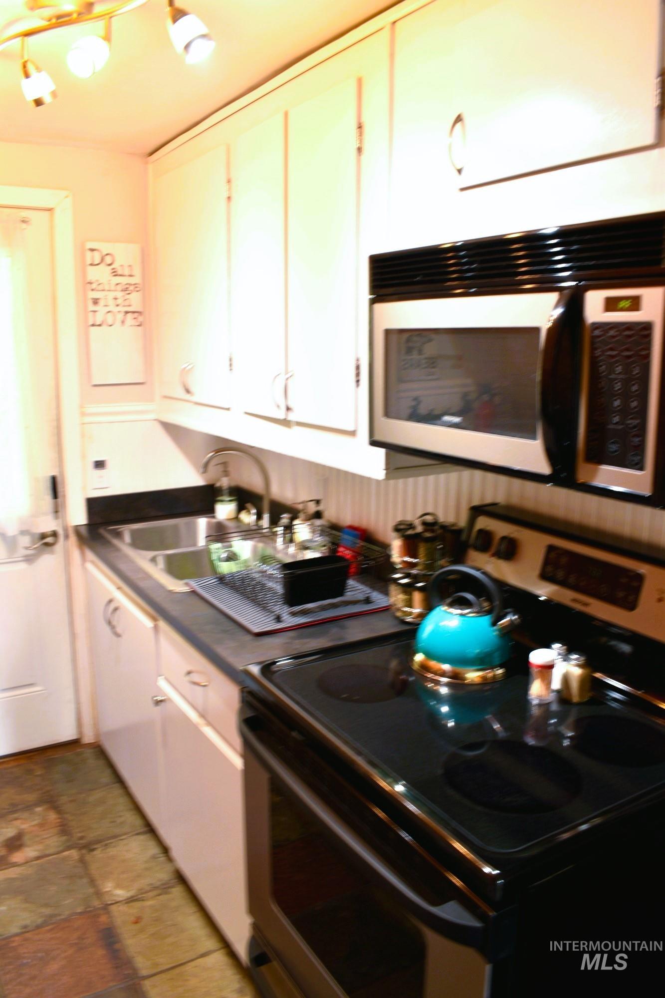 Kitchen featuring white cabinetry, a stainless steel sink, black countertops, a built-in microwave, and a black electric range with a glass cooktop