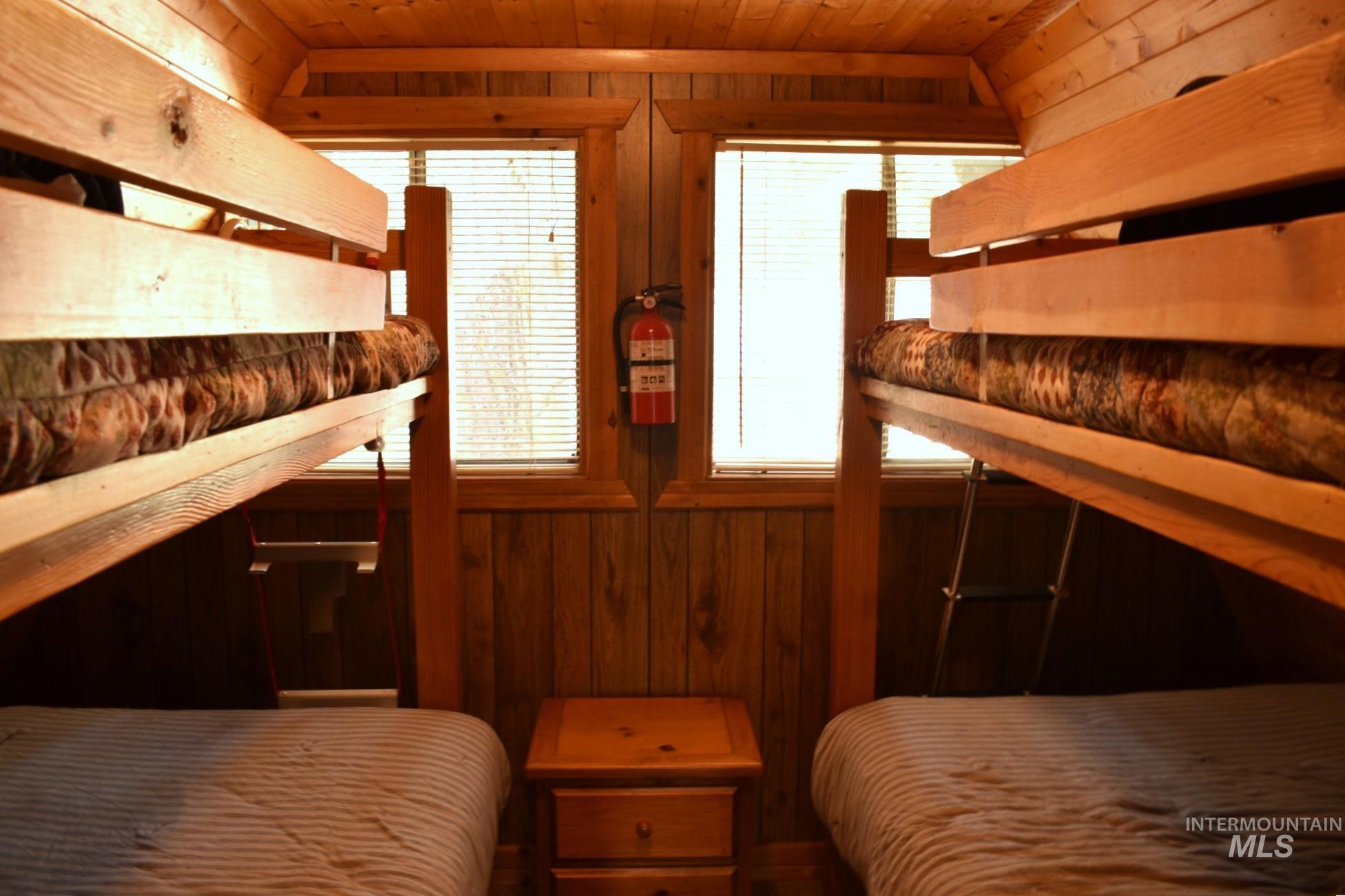 Wood-paneled room featuring two bunk beds with built-in ladders, wood-finish flooring, and a central wood nightstand with drawers