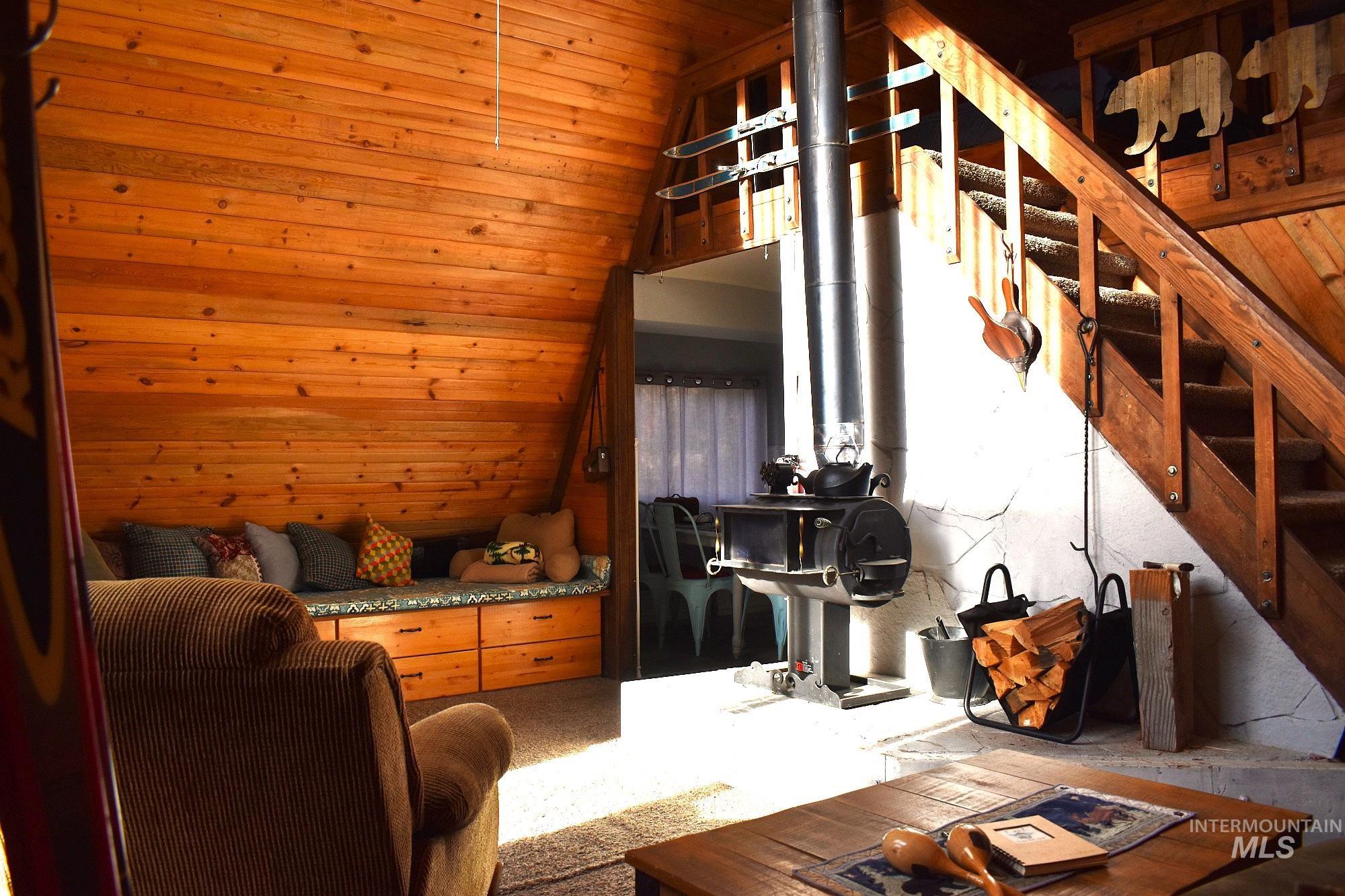 Wood-paneled interior featuring an exposed wood-burning stove with a metal flue, a built-in window bench with drawer storage, and a natural wood staircase with a matching railing