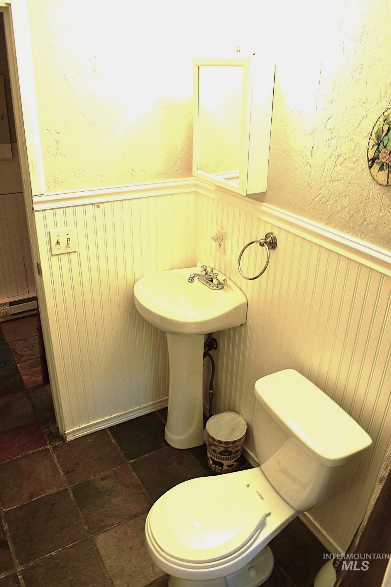 Bathroom featuring a pedestal sink, white toilet, and multi-toned stone tile flooring