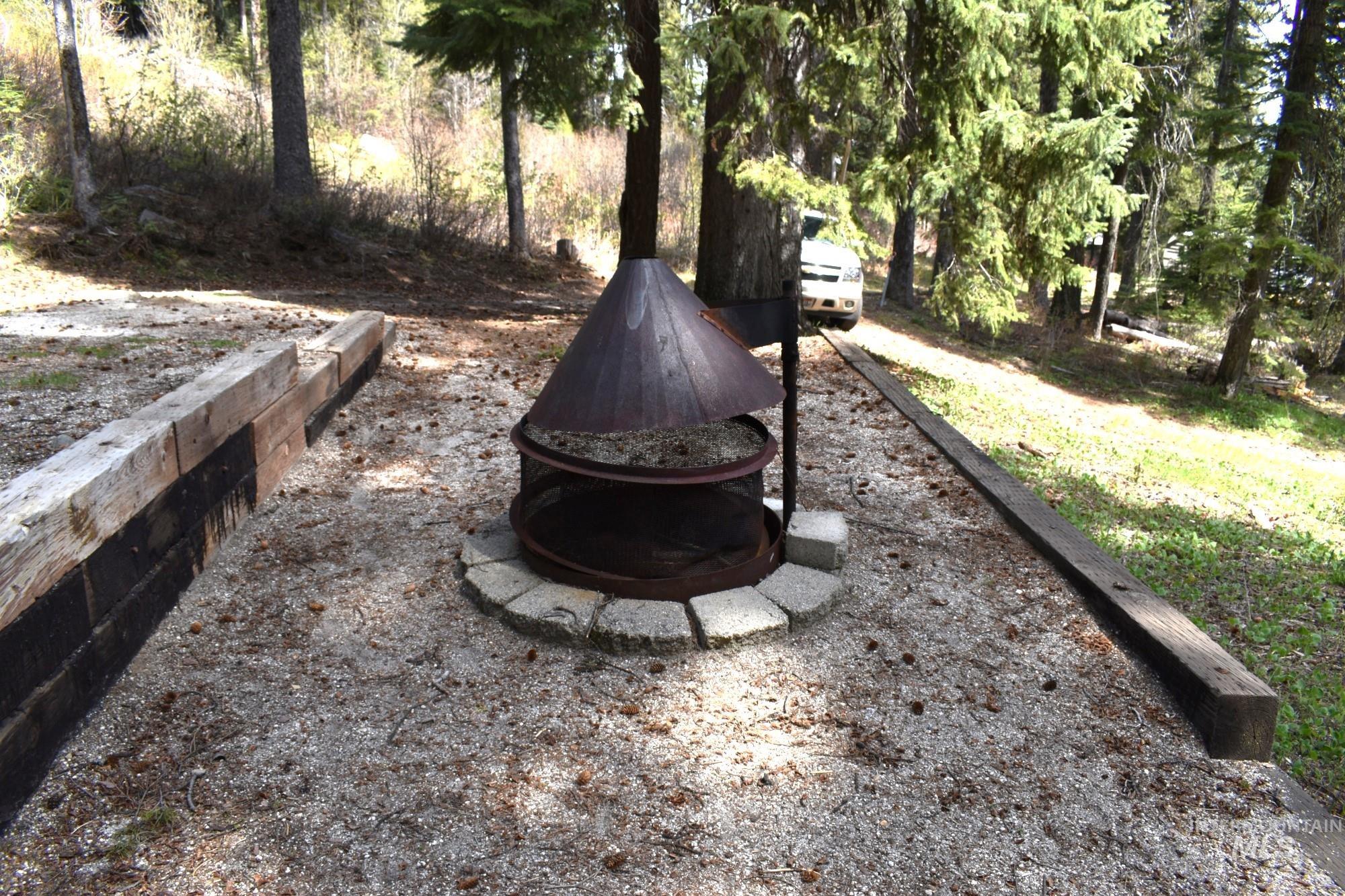 Outdoor fire pit with a conical metal top, set on a stone base within a gravel-covered area