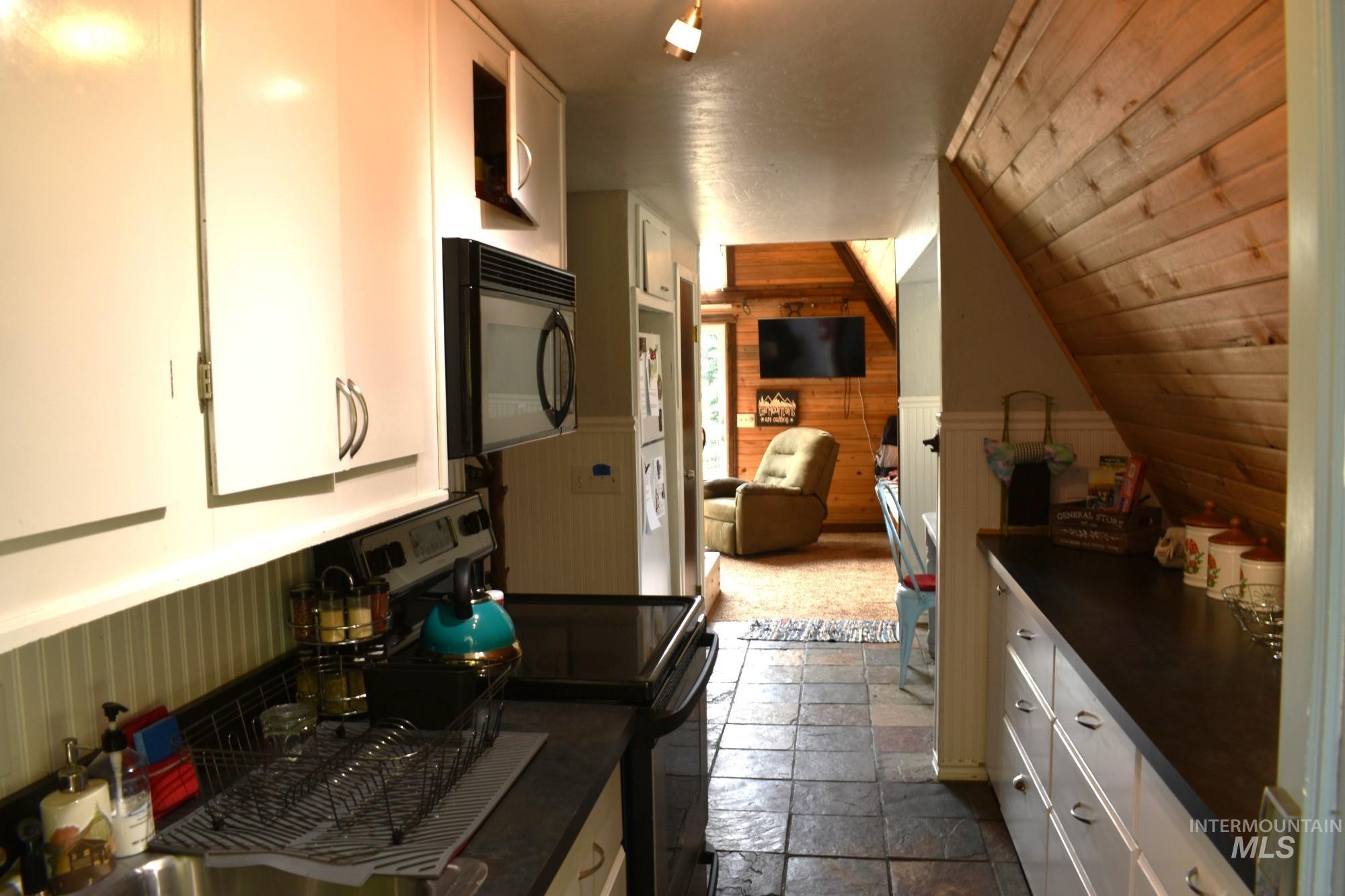 Galley kitchen featuring white cabinetry, dark countertops, and a full suite of appliances