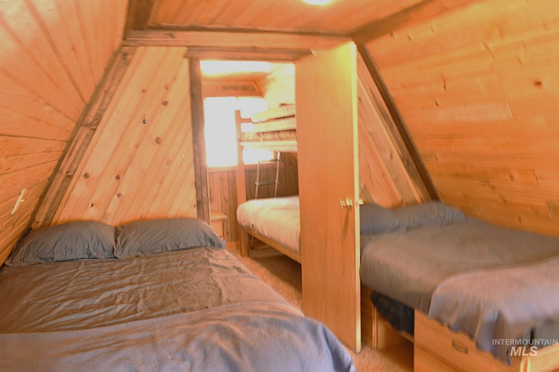 Sloped wood-paneled walls with exposed wood beams, featuring three integrated sleeping areas