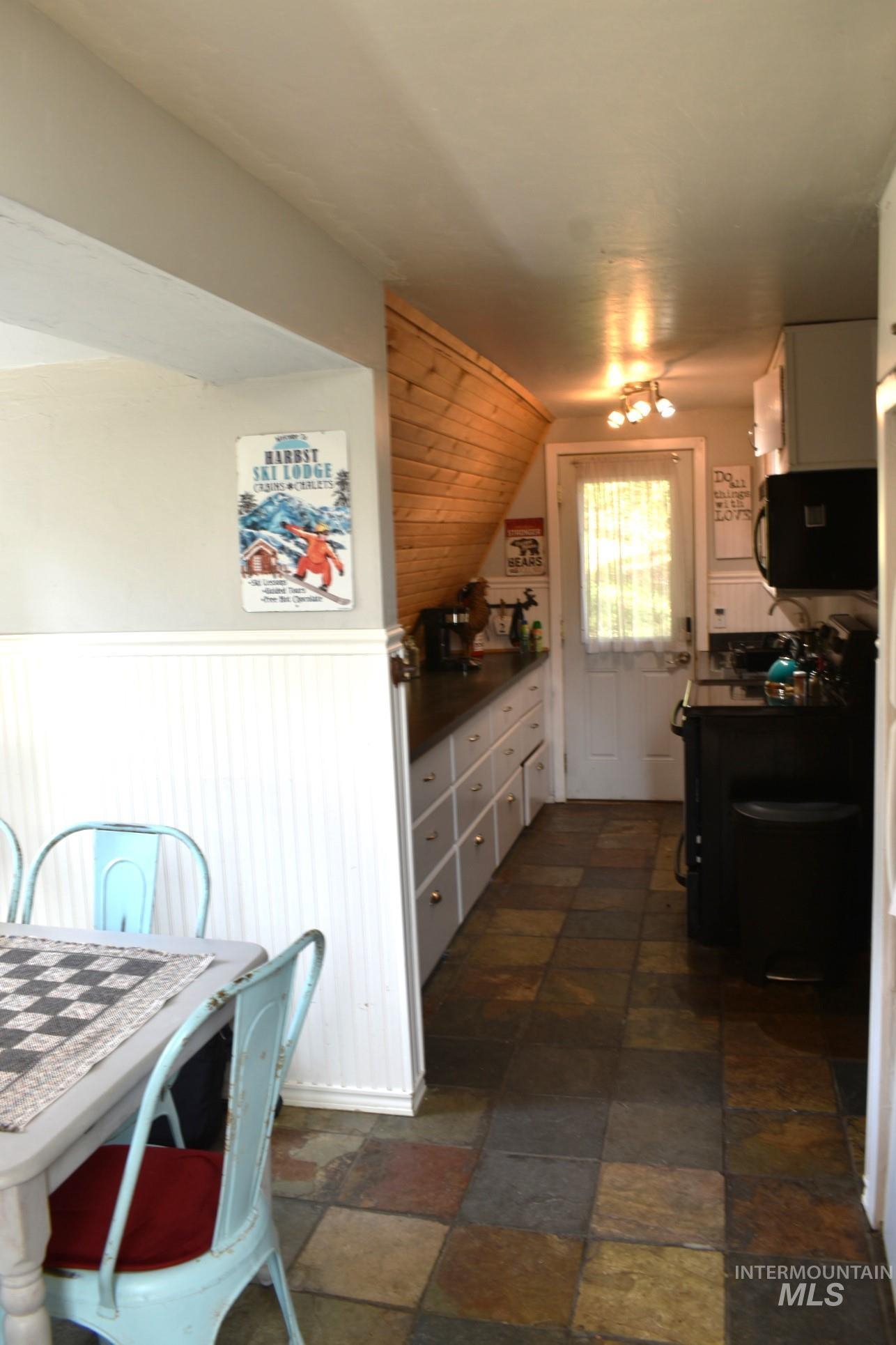 Kitchen featuring multi-colored natural stone tile flooring, a white paneled half-wall, and wood-paneled wall details