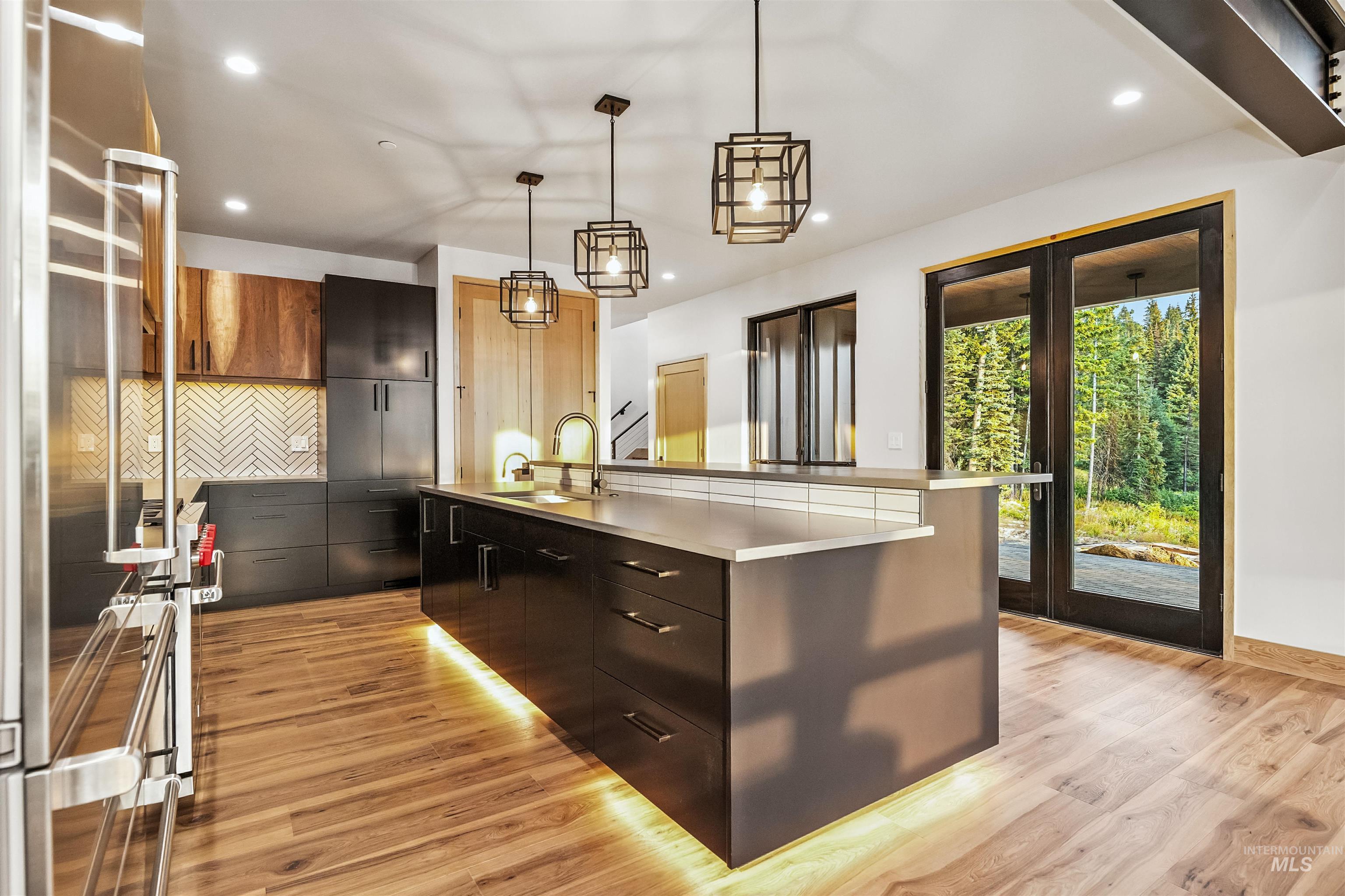 Kitchen featuring appliances with stainless steel finishes, pendant lighting, a center island with sink, light wood-style flooring, and recessed lighting