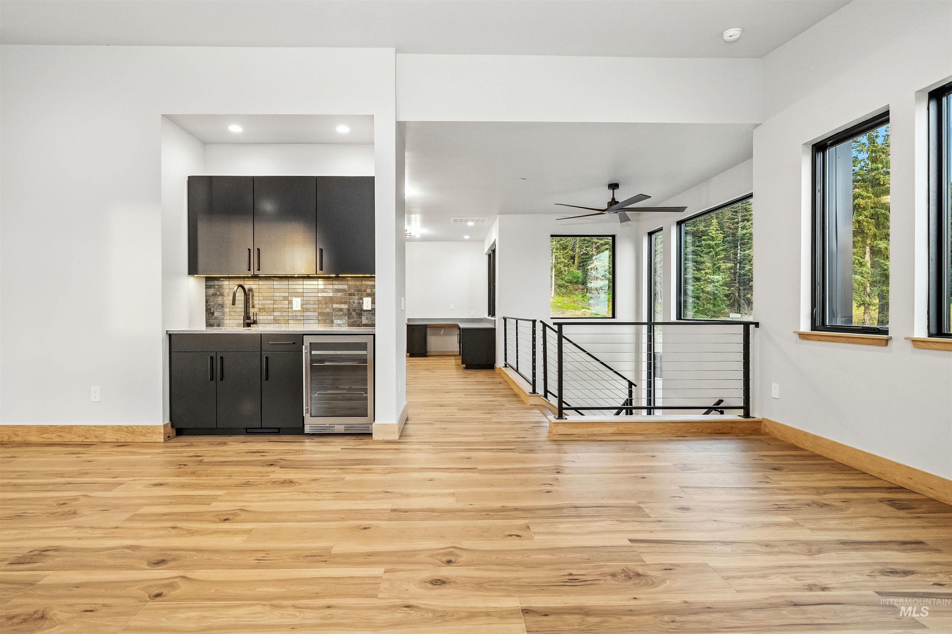 Indoor wet bar with dark cabinetry, backsplash, wine cooler, light wood-style floors, and recessed lighting