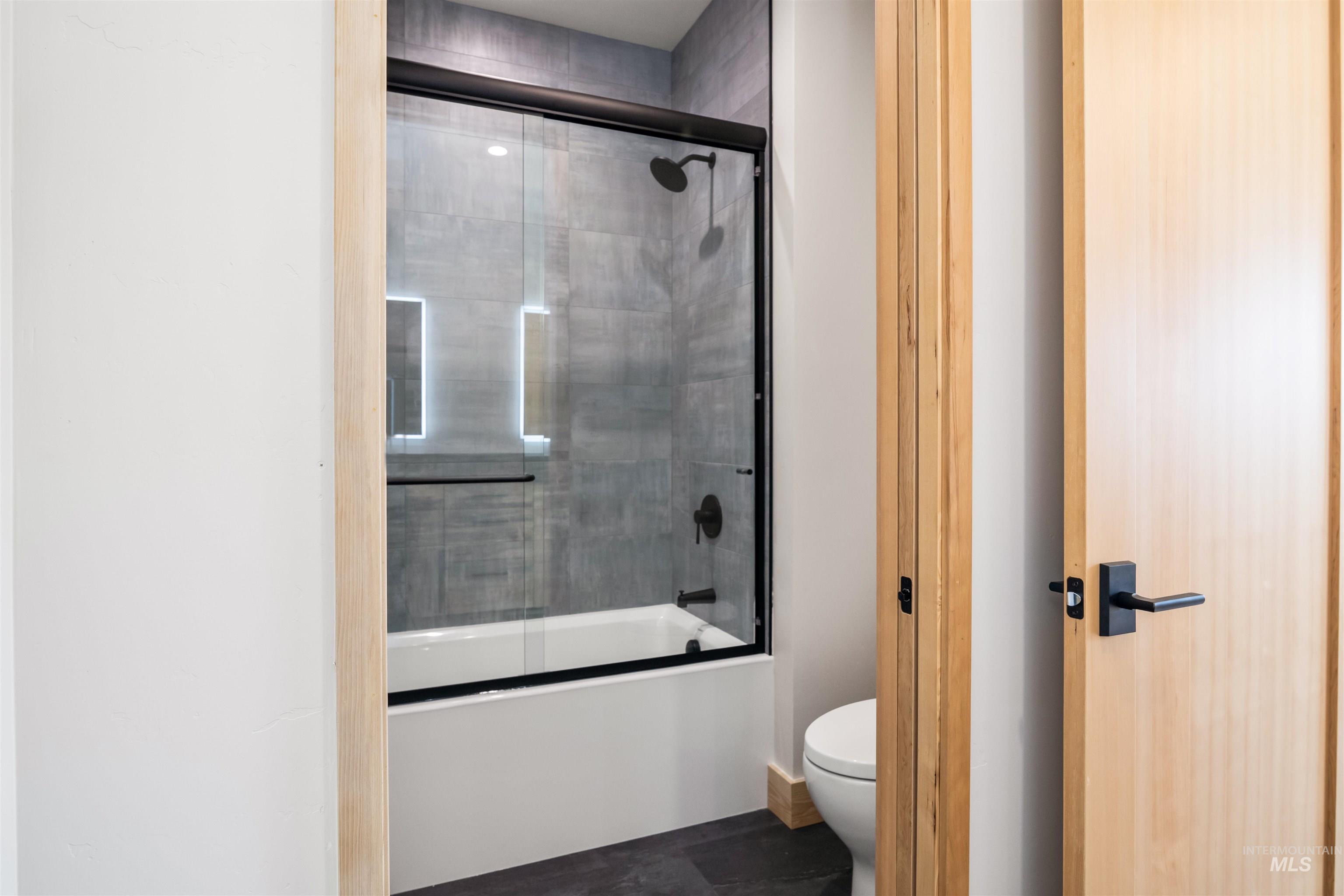 Full bath featuring bath / shower combo with glass door and toilet