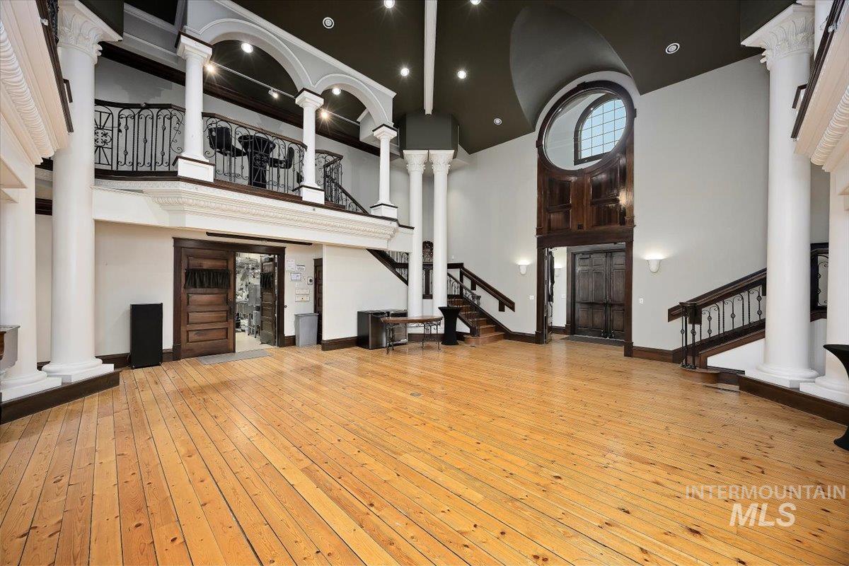 Unfurnished living room with stairway, ornate columns, light wood-style flooring, high vaulted ceiling, and recessed lighting