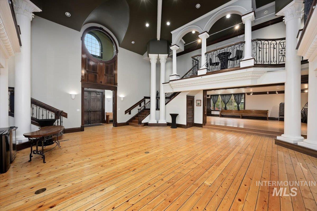 Living room with decorative columns, light wood finished floors, stairway, a towering ceiling, and recessed lighting