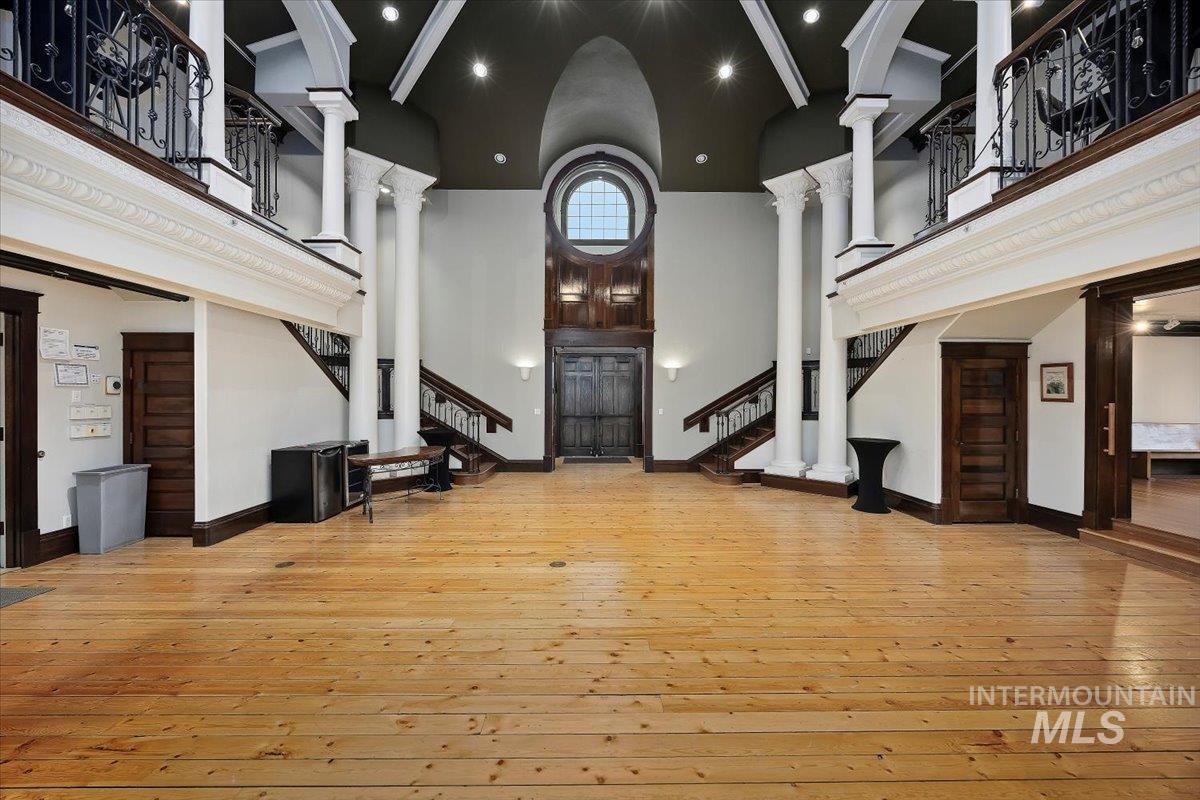 Unfurnished living room featuring light wood finished floors, decorative columns, stairway, a towering ceiling, and recessed lighting
