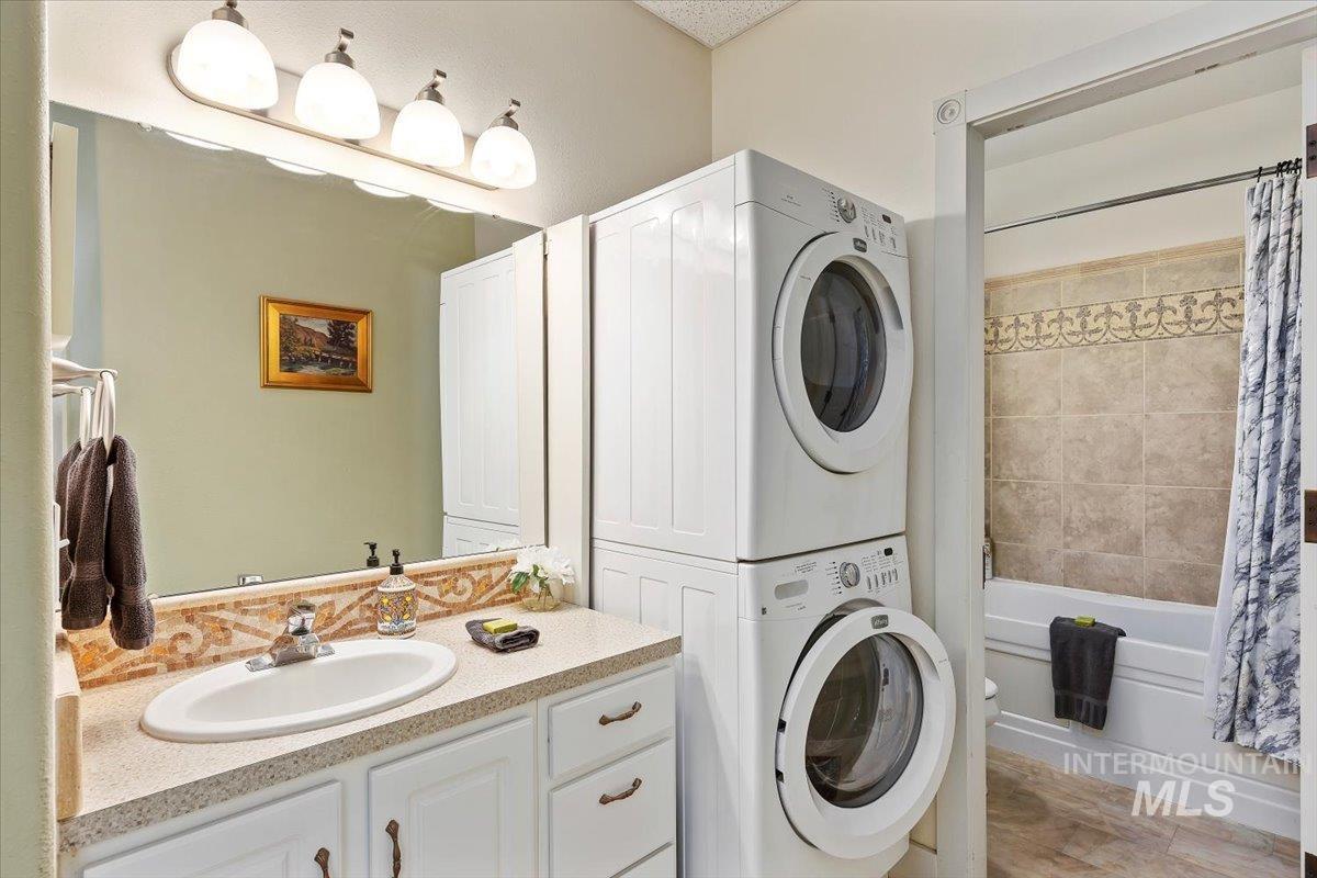 Full bath featuring shower / bath combo, vanity, stacked washer / drying machine, and light wood-style flooring