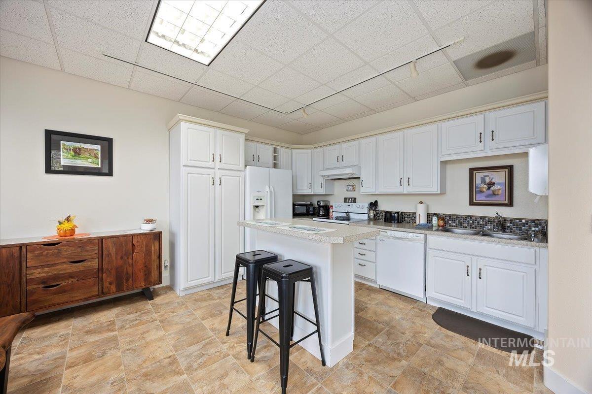 Kitchen with a kitchen breakfast bar, a drop ceiling, white cabinets, light countertops, and white appliances