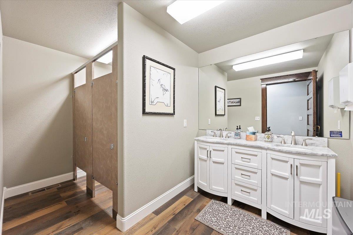 Full bathroom featuring double vanity, dark wood-style flooring, and a textured ceiling