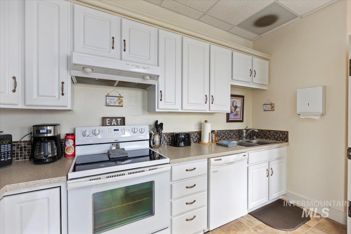 Kitchen featuring white appliances, white cabinetry, under cabinet range hood, light countertops, and a drop ceiling