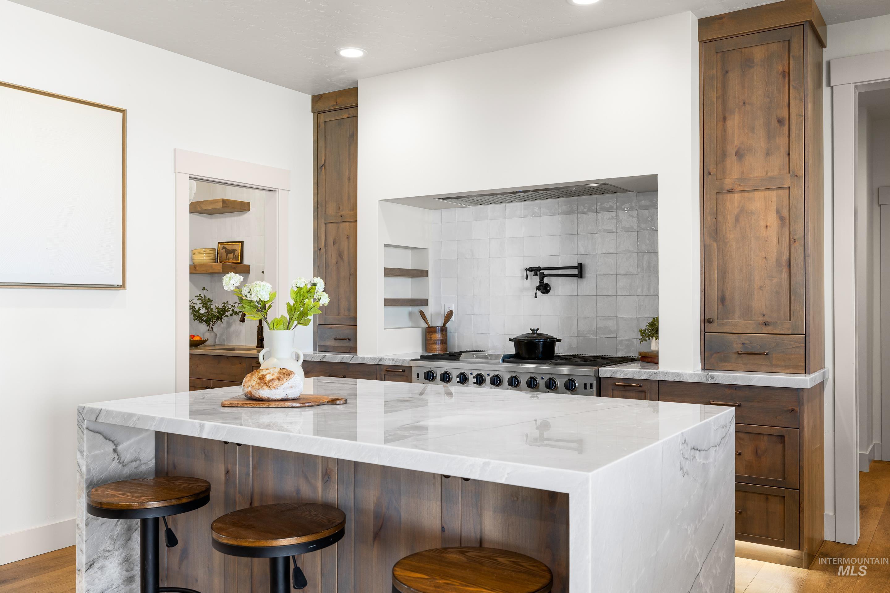 Kitchen featuring light wood-type flooring, decorative backsplash, light stone countertops, a breakfast bar, and a center island