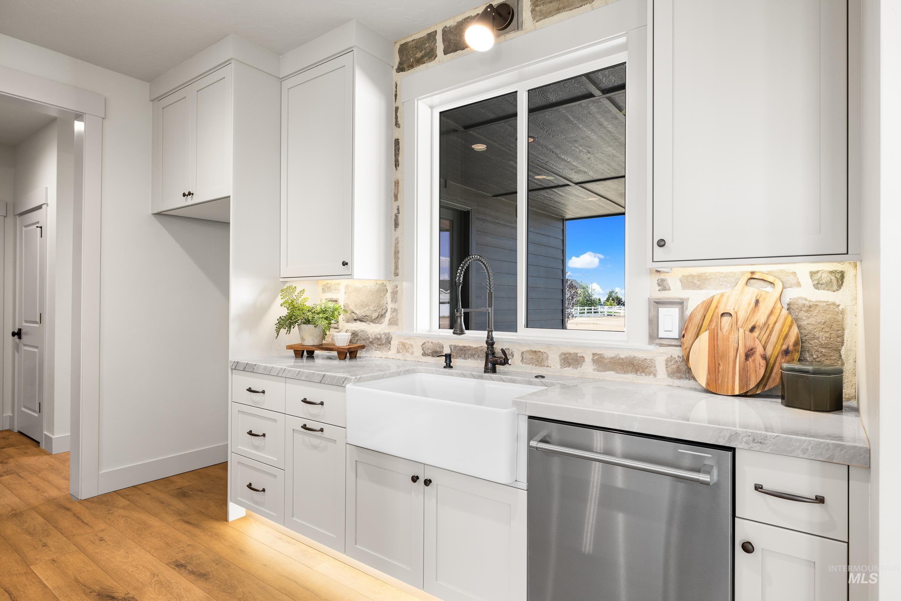 Kitchen with stainless steel dishwasher, light wood-type flooring, backsplash, and white cabinetry