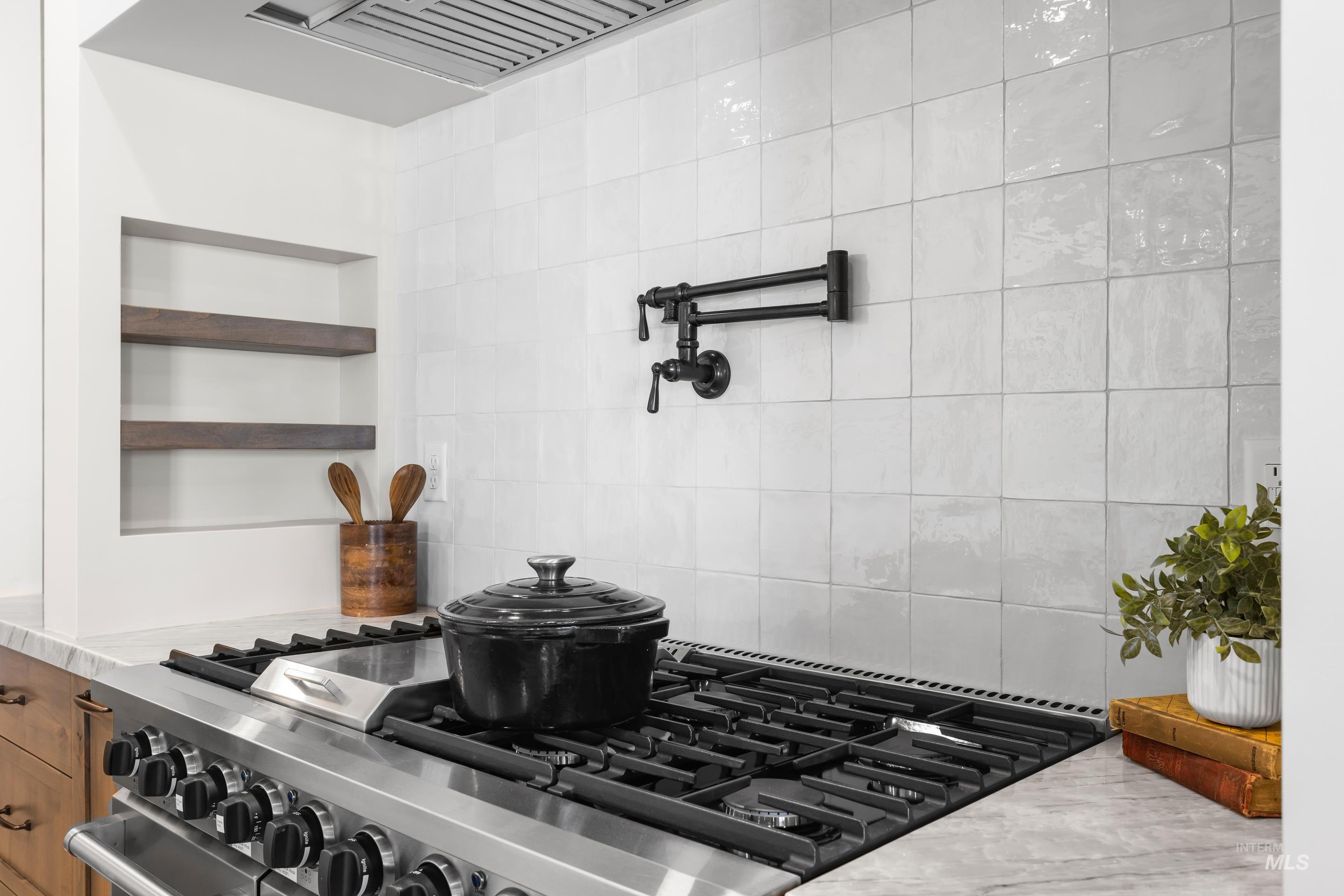 Kitchen view of pot filler, tasteful backsplash, open shelves, brown cabinets, and premium range hood