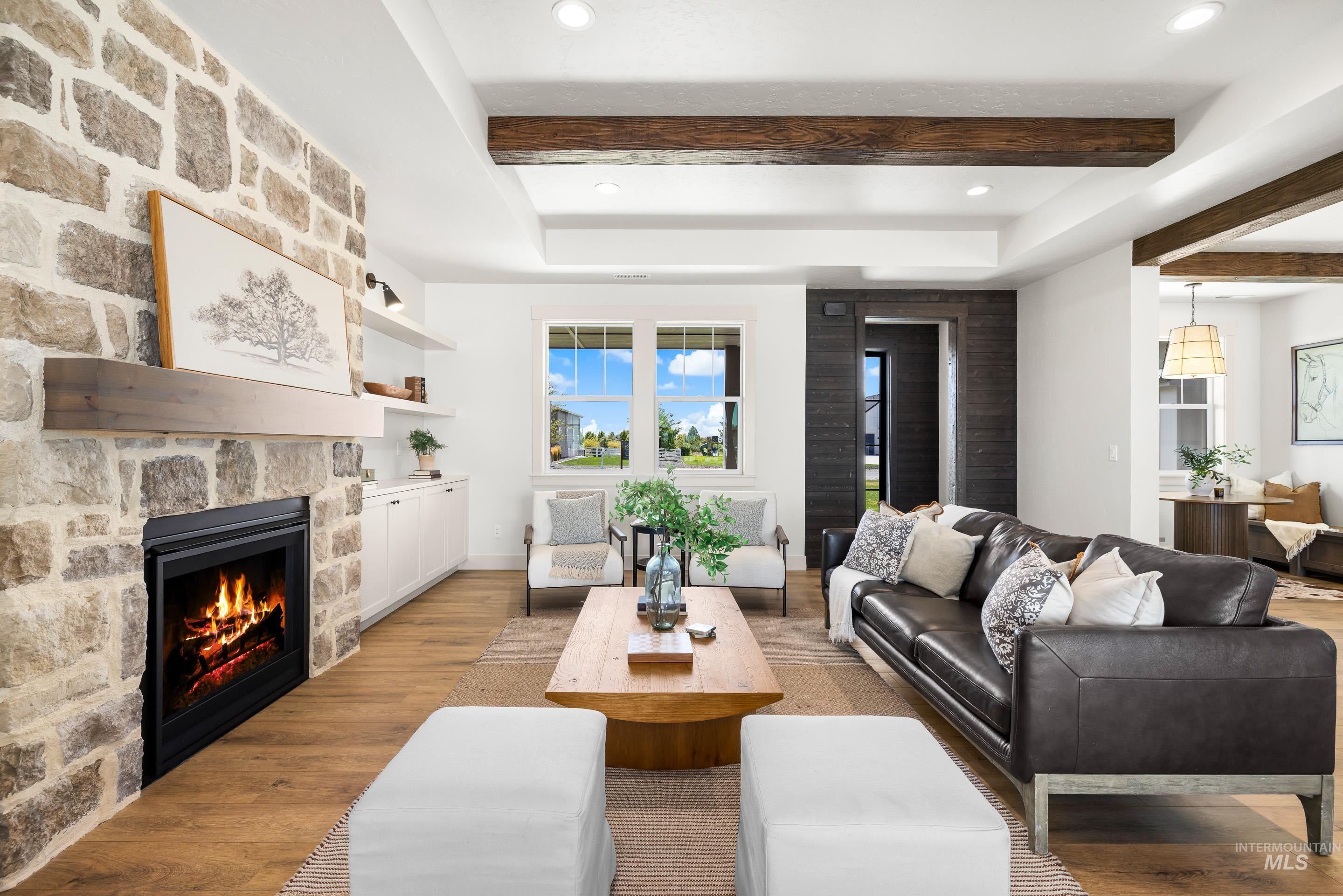 Living area with light wood-style flooring, beam ceiling, a fireplace, and a raised ceiling
