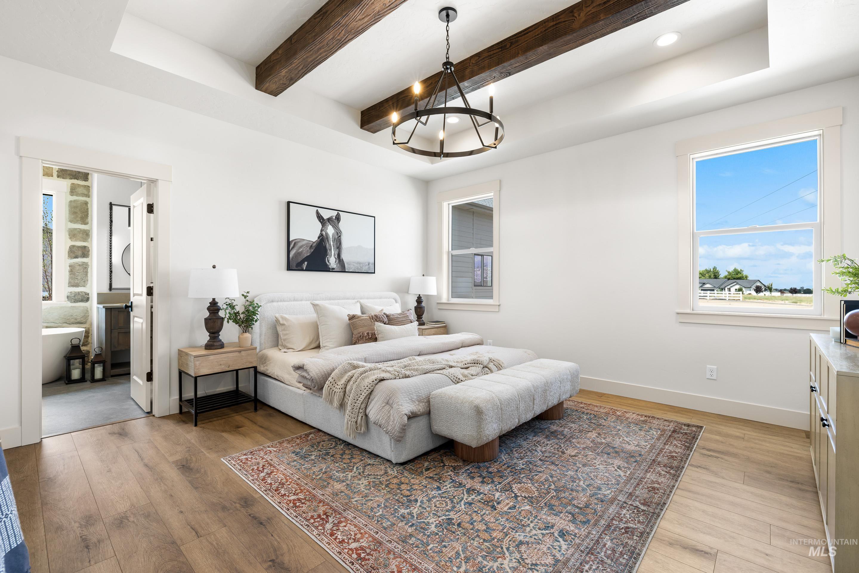 Bedroom with multiple windows, light wood-style floors, a chandelier, beamed ceiling, and connected bathroom