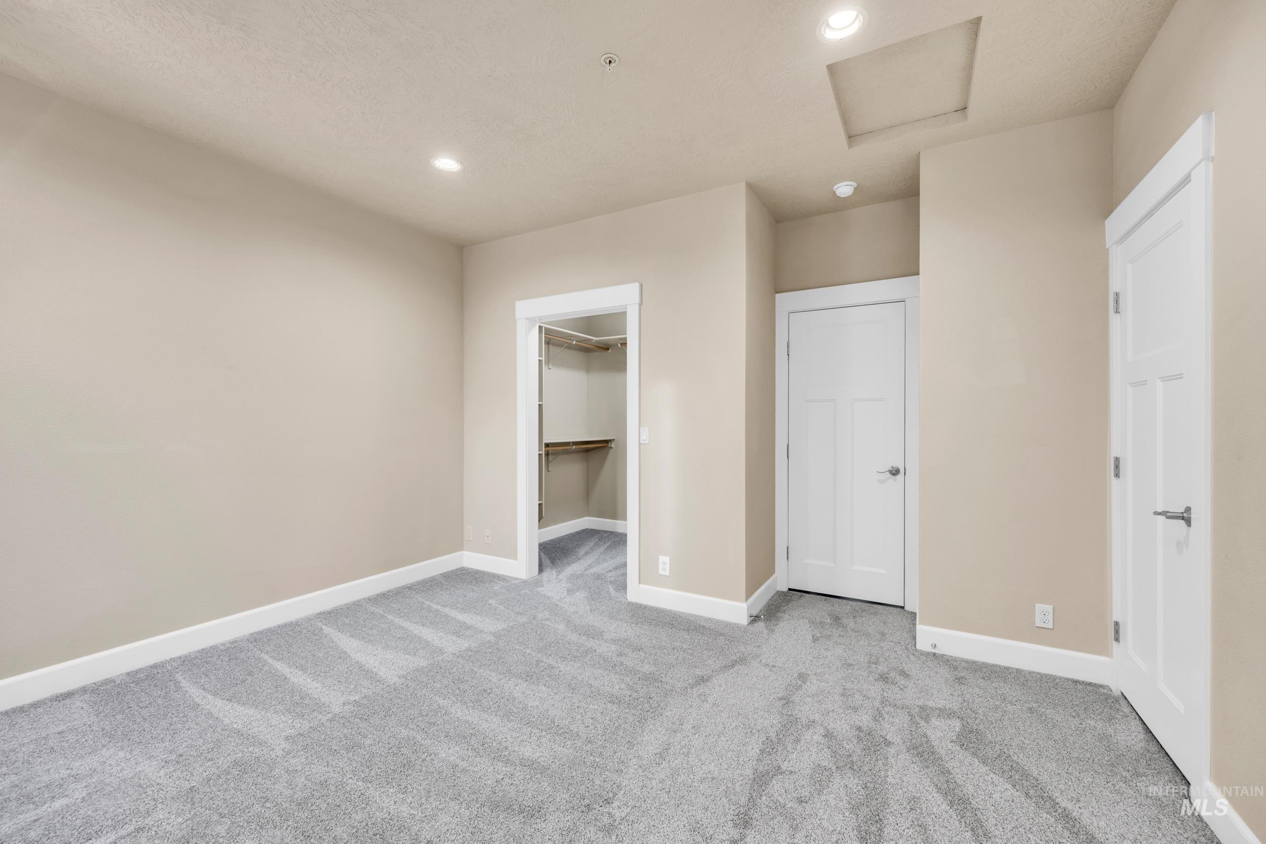 Unfurnished bedroom featuring attic access, light carpet, recessed lighting, and a walk in closet